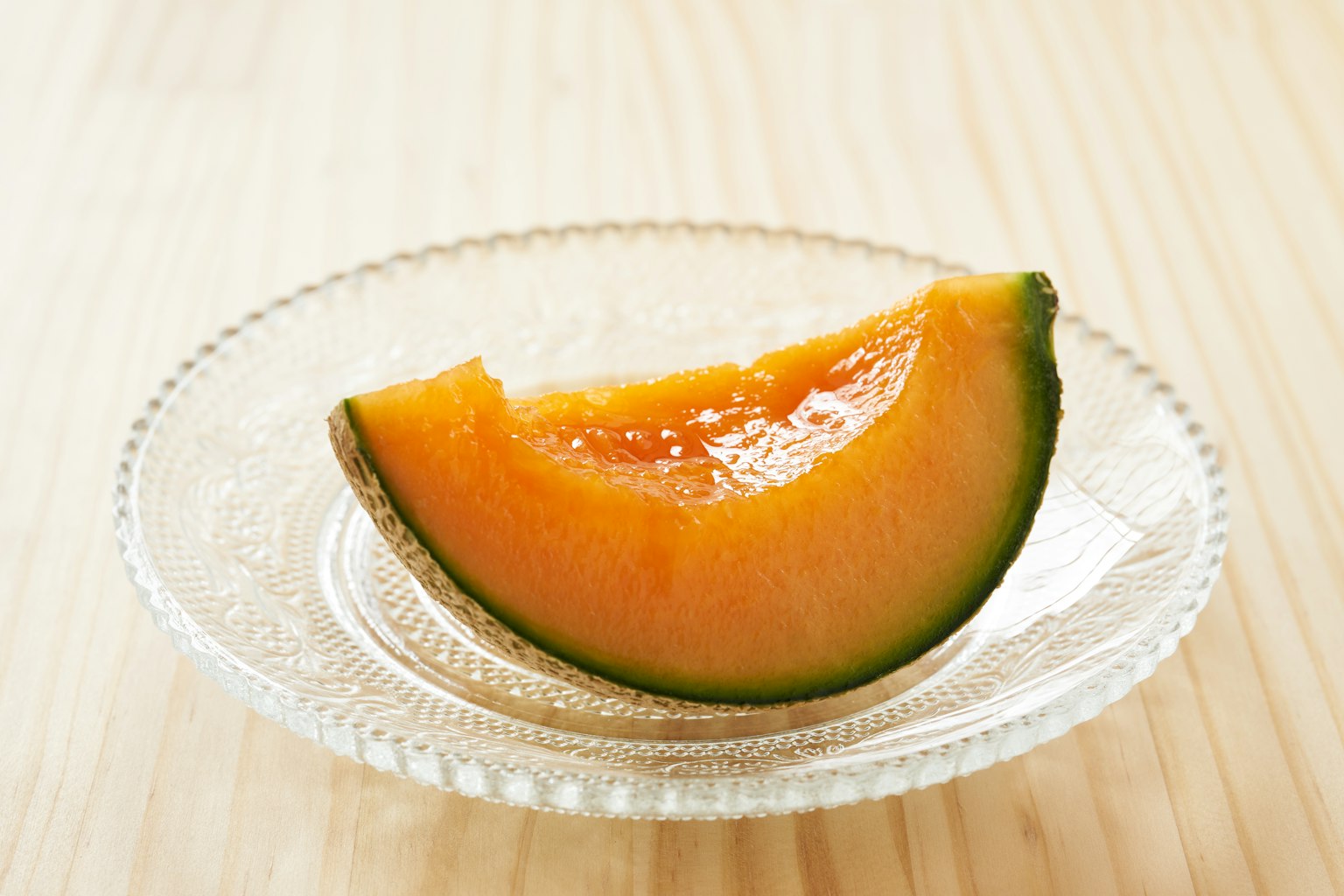 Eine Scheibe reifer Melone auf einem klaren Teller auf einer Holzoberfläche