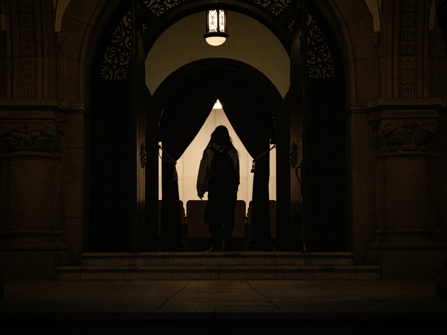 Silhouette einer Person in einem dunklen Bogen mit einem Vorhang im Hintergrund
