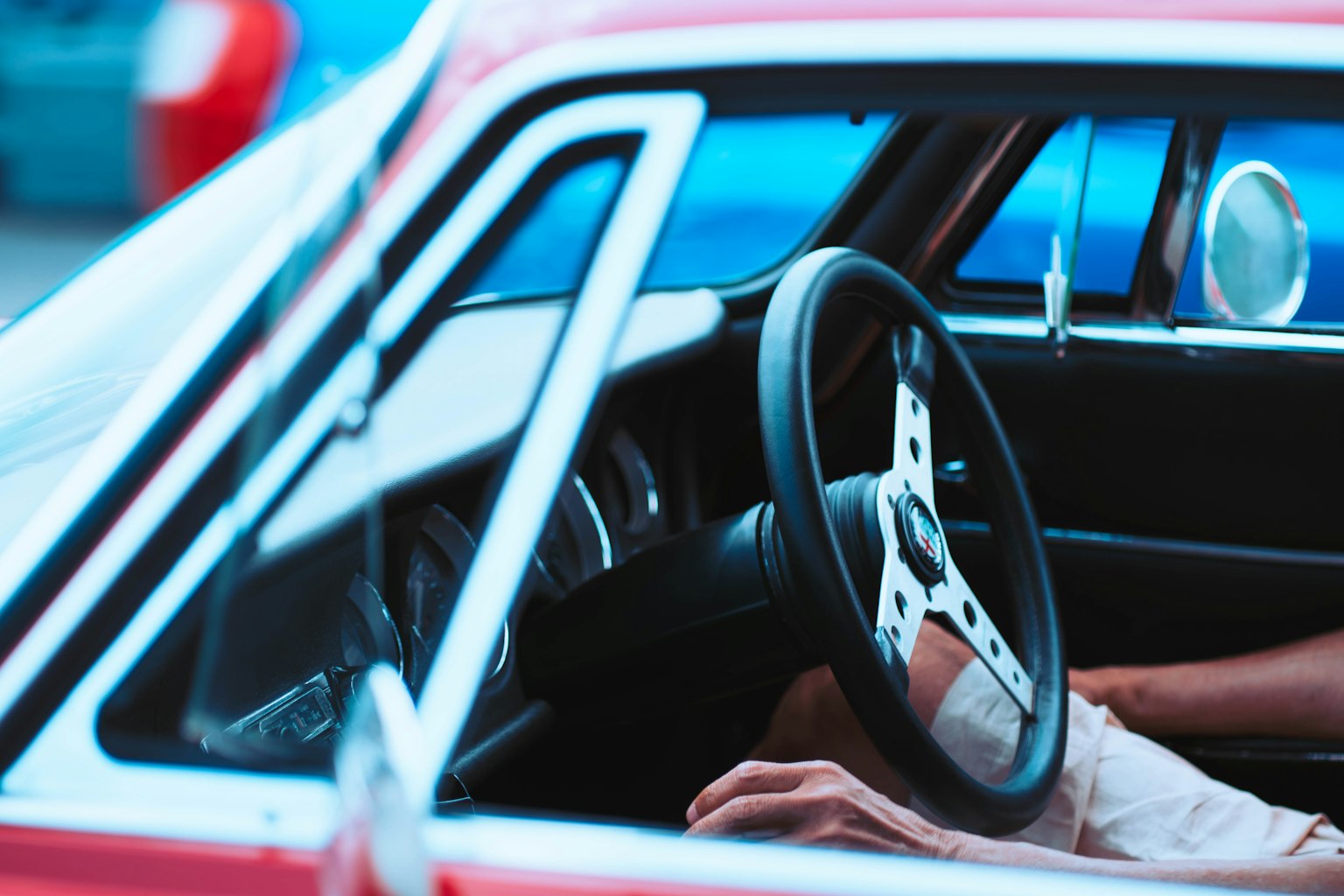 Primer plano de una mano en el volante de un auto clásico rojo