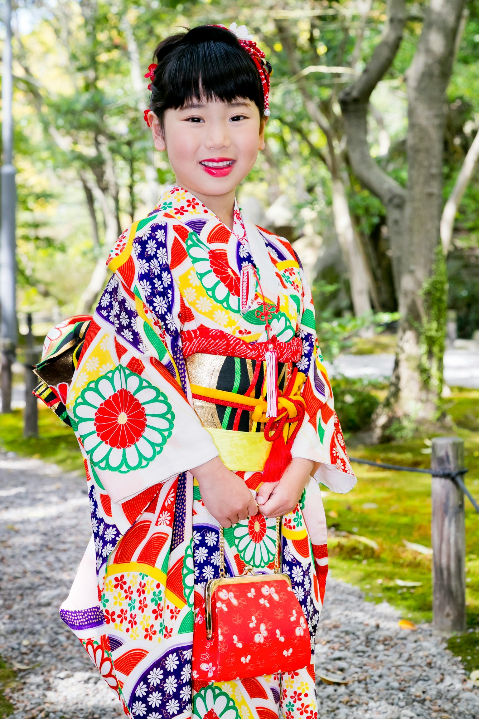 ผู้หญิงในชุดกิโมโนสีสันสดใสยิ้มอยู่ในบรรยากาศธรรมชาติ