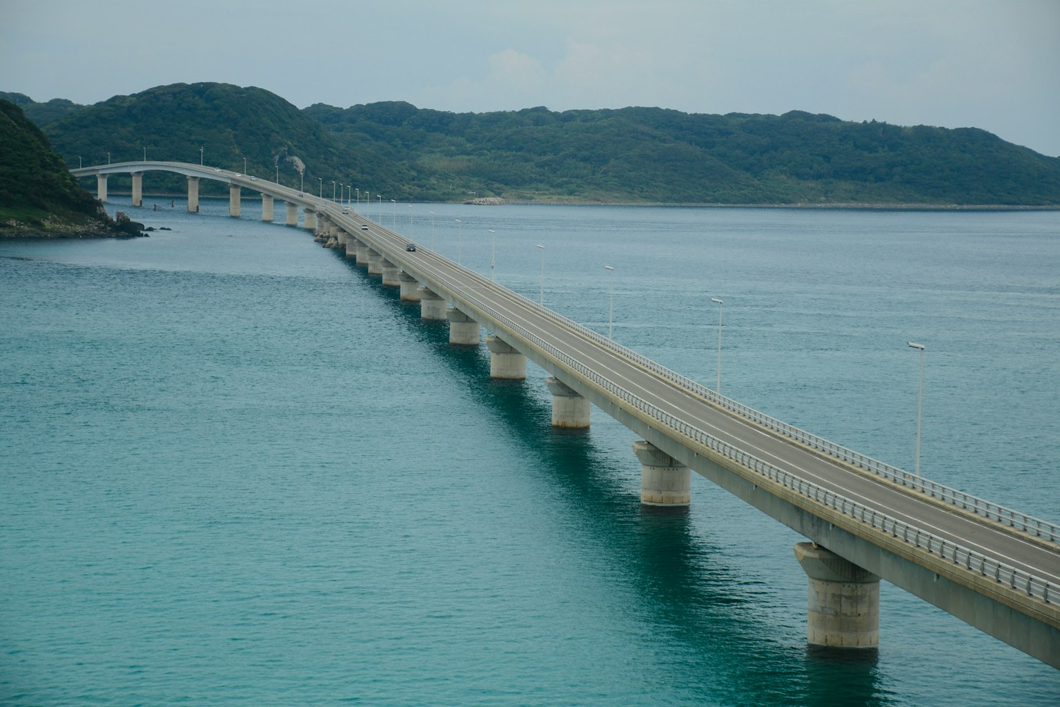 Un largo puente sobre agua azul con islas verdes al fondo