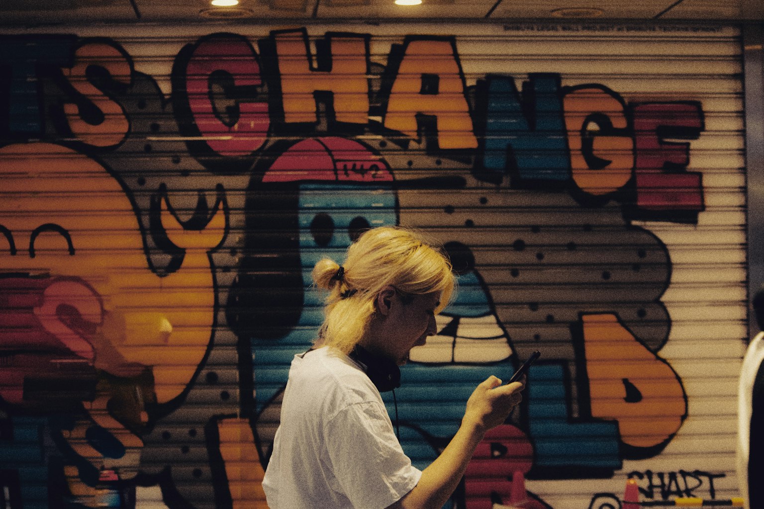 Seorang wanita menggunakan smartphone di depan mural grafiti berwarna-warni