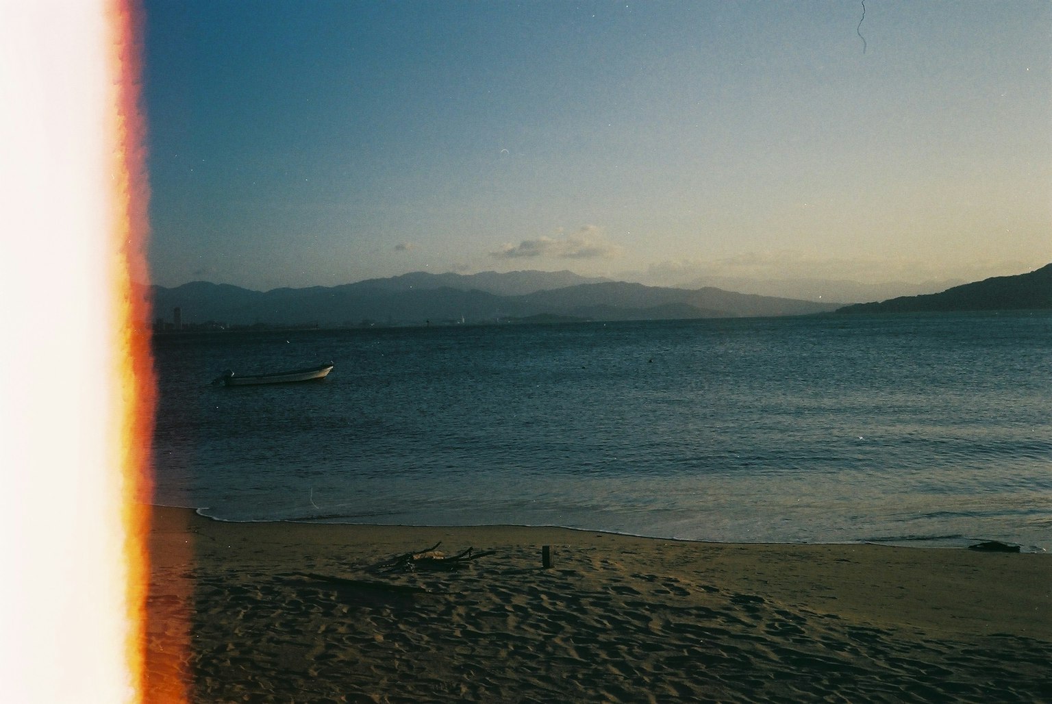 Spiaggia al tramonto con montagne sullo sfondo e una barca in acqua