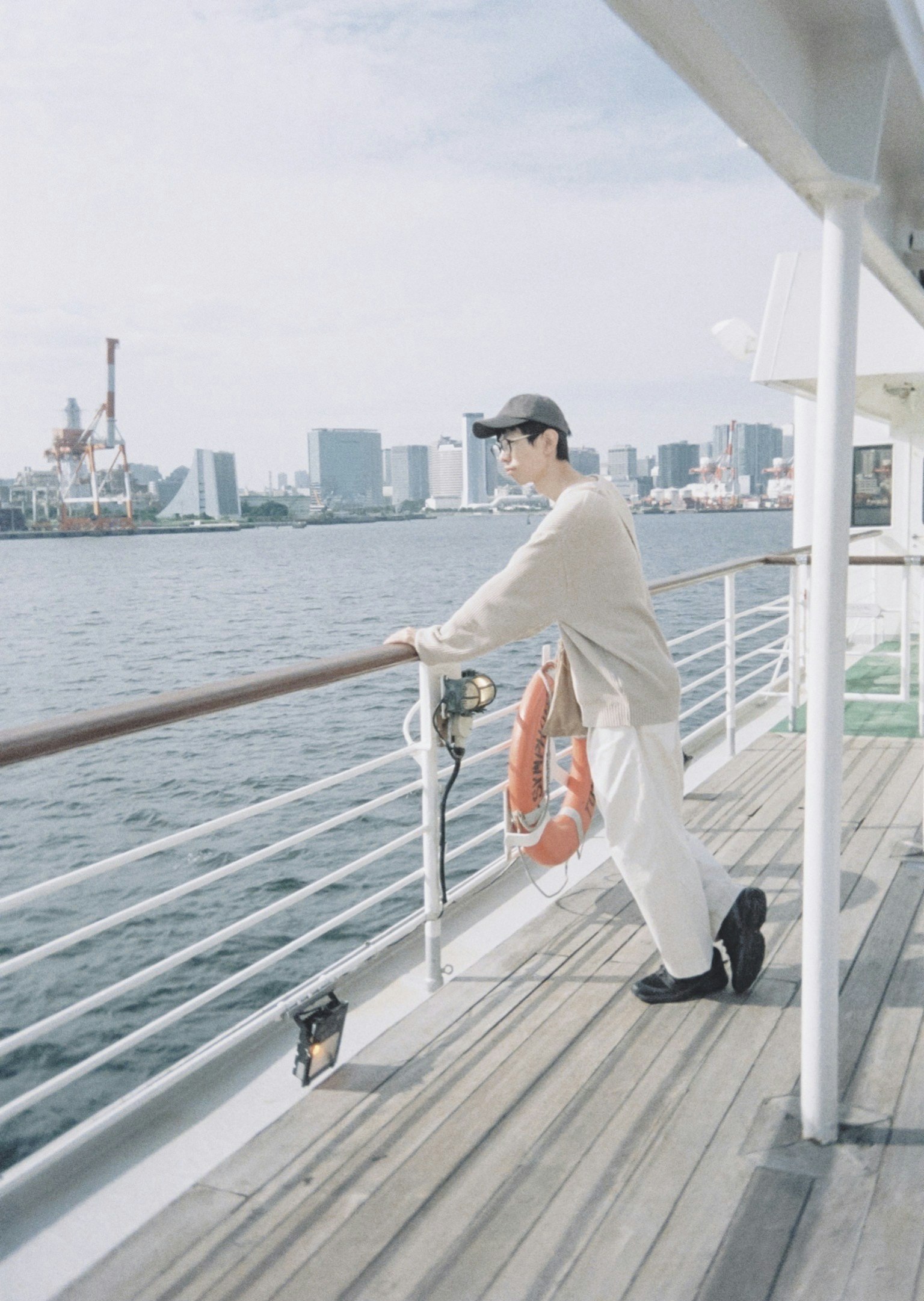 คนยืนพิงราวมองทะเลพร้อมกับเส้นขอบฟ้าของเมืองในพื้นหลัง