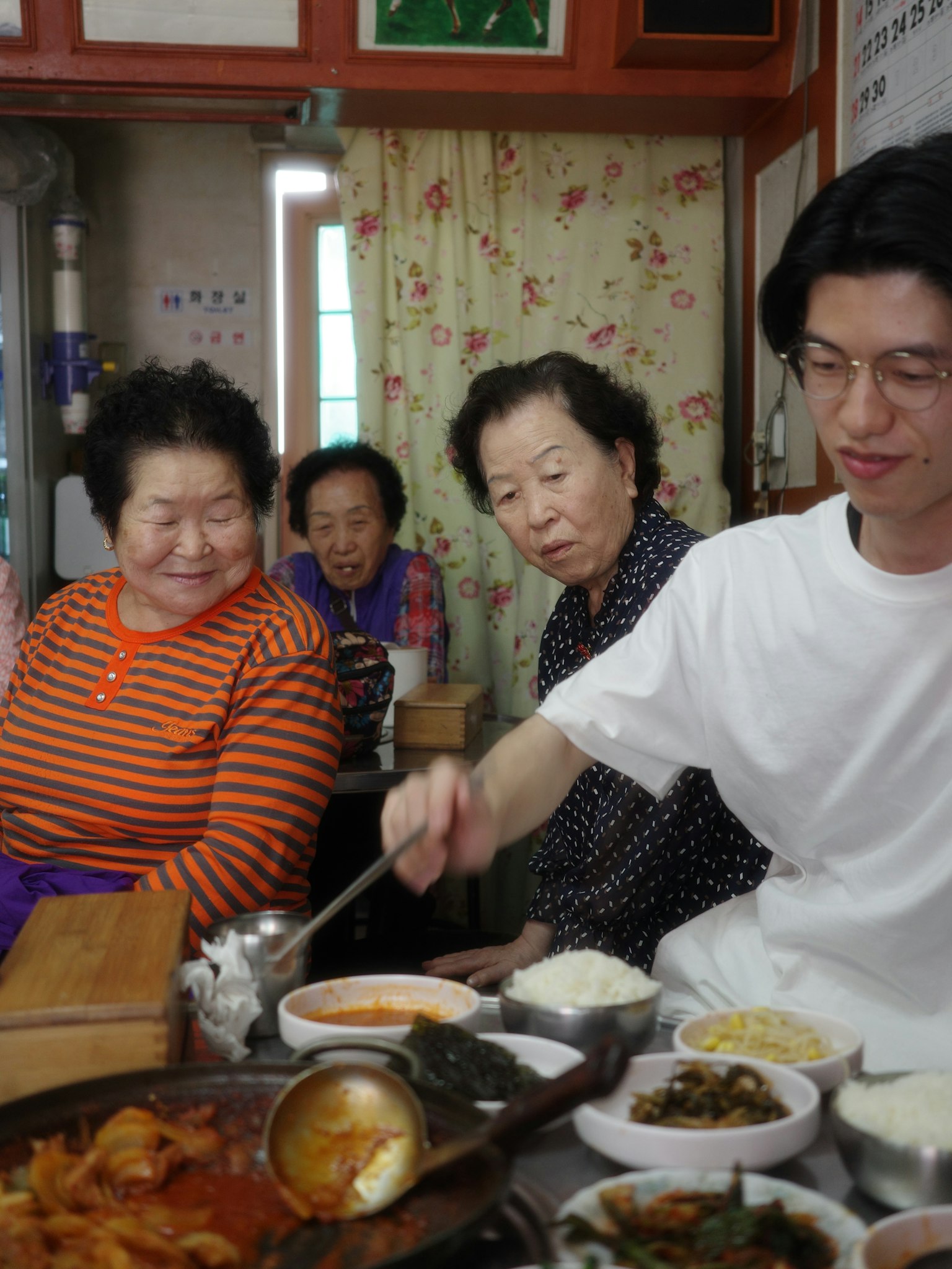 Group of elderly women and a young man enjoying a meal Traditional Korean dishes on the table