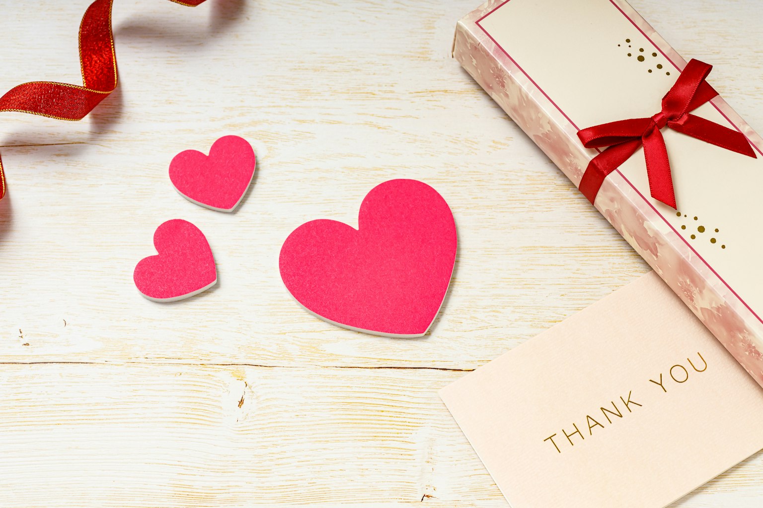 Three pink heart shapes and a gift box with a ribbon on a wooden surface