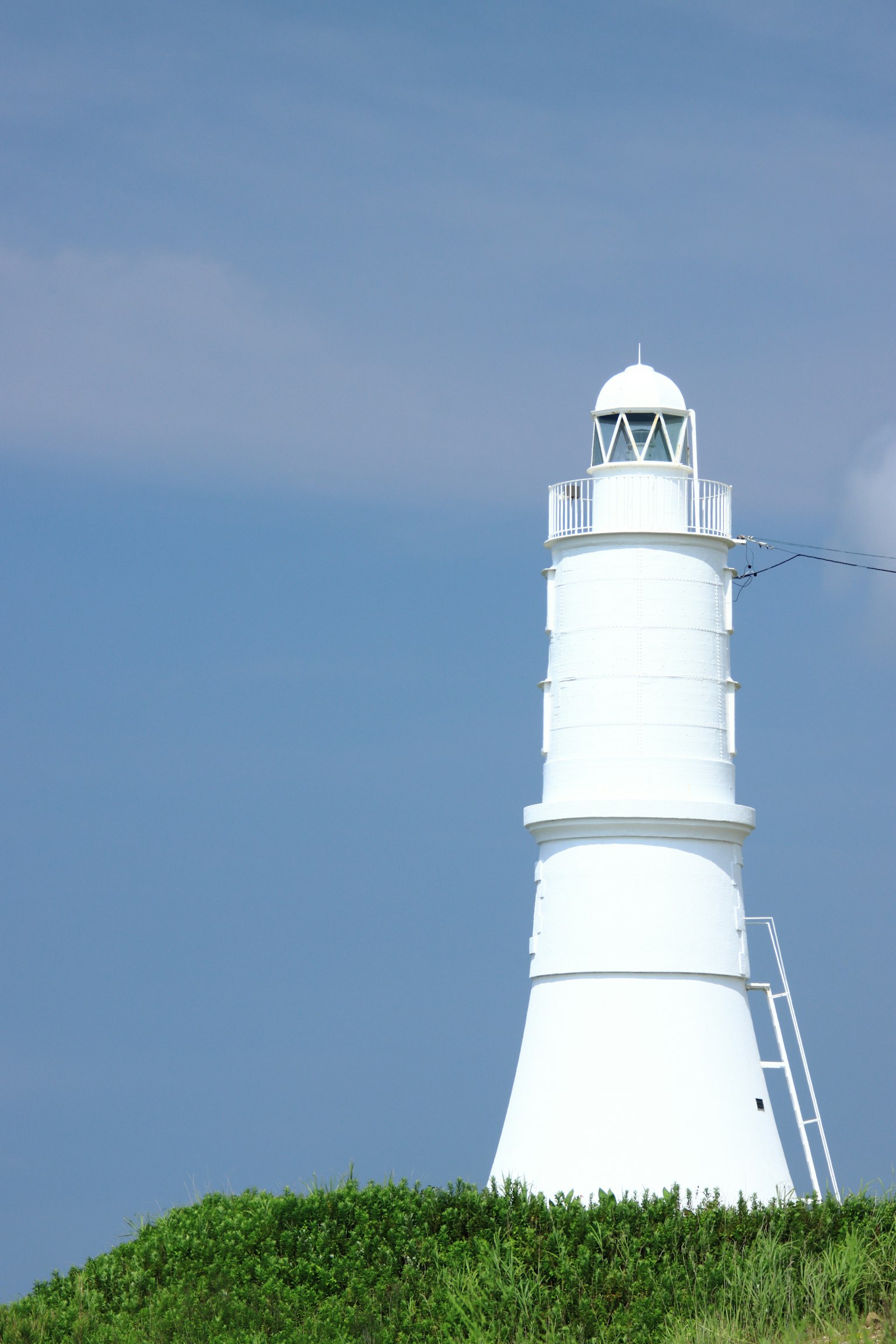 Un faro bianco che si erge su una collina verde sotto un cielo blu