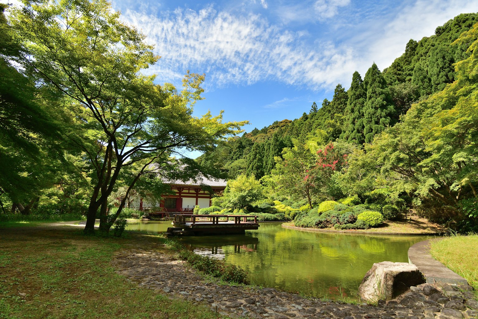 Jardín japonés pintoresco con estanque y árboles bajo un cielo azul