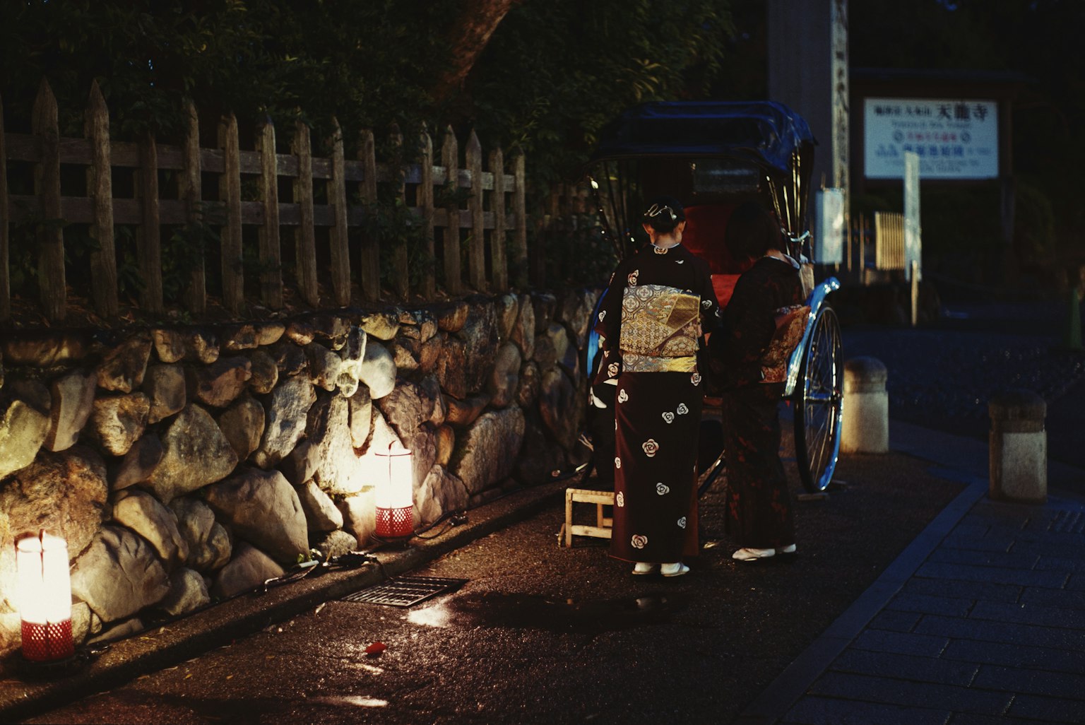 คนขับรถลากนั่งอยู่บนถนนในตอนกลางคืนพร้อมกำแพงหินและโคมไฟ