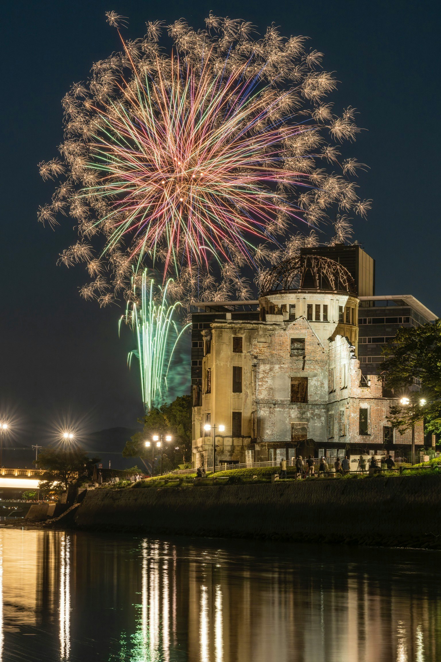 Bunte Feuerwerke erhellen den Nachthimmel über einem historischen Gebäude am Fluss