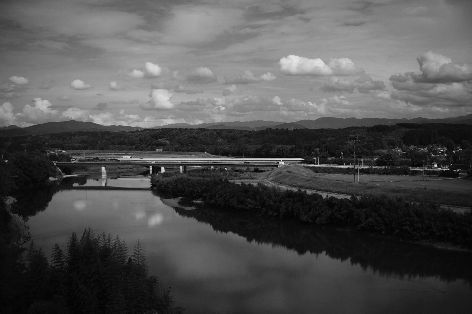 Foto lanskap hitam putih menampilkan sungai dan jembatan
