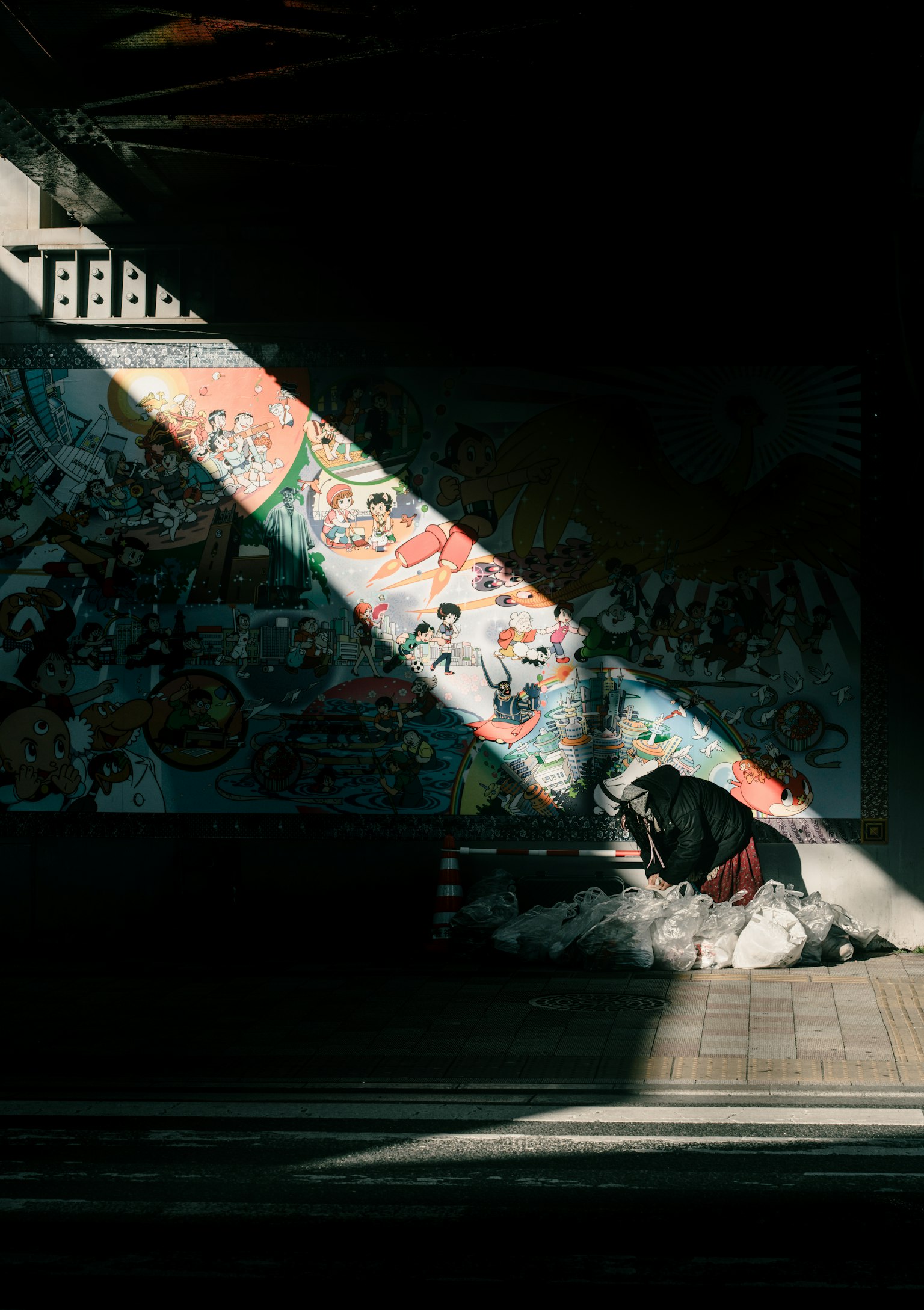 A person huddled by a pile of trash in a dark area with colorful murals