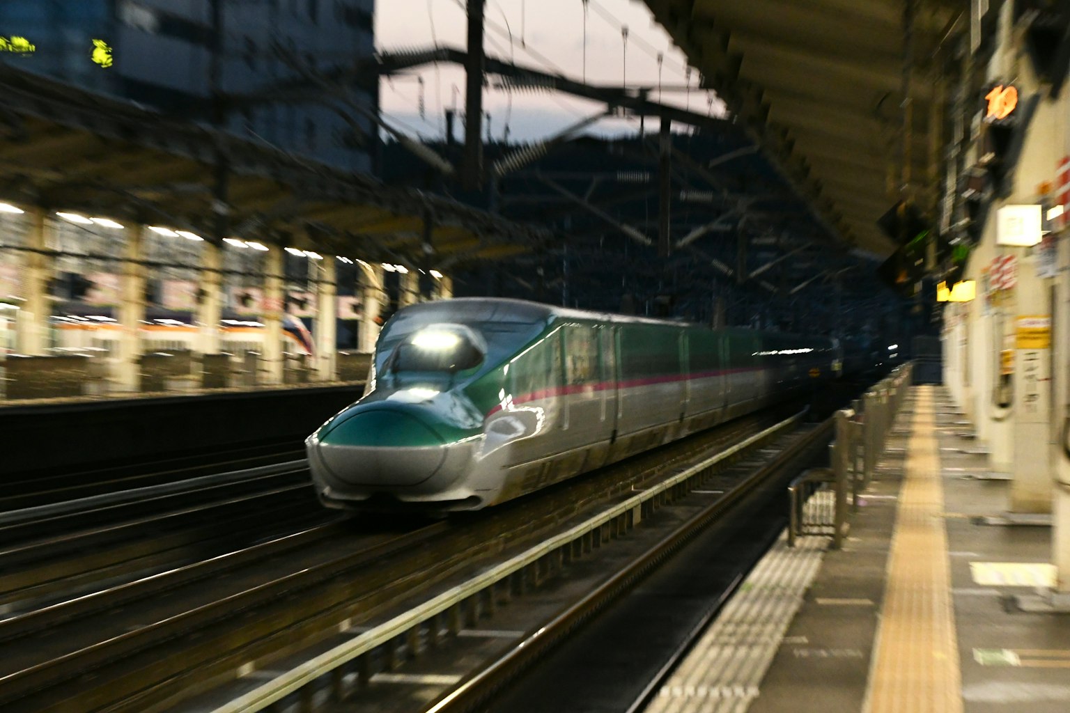 Kereta cepat Shinkansen melaju melalui stasiun di malam hari