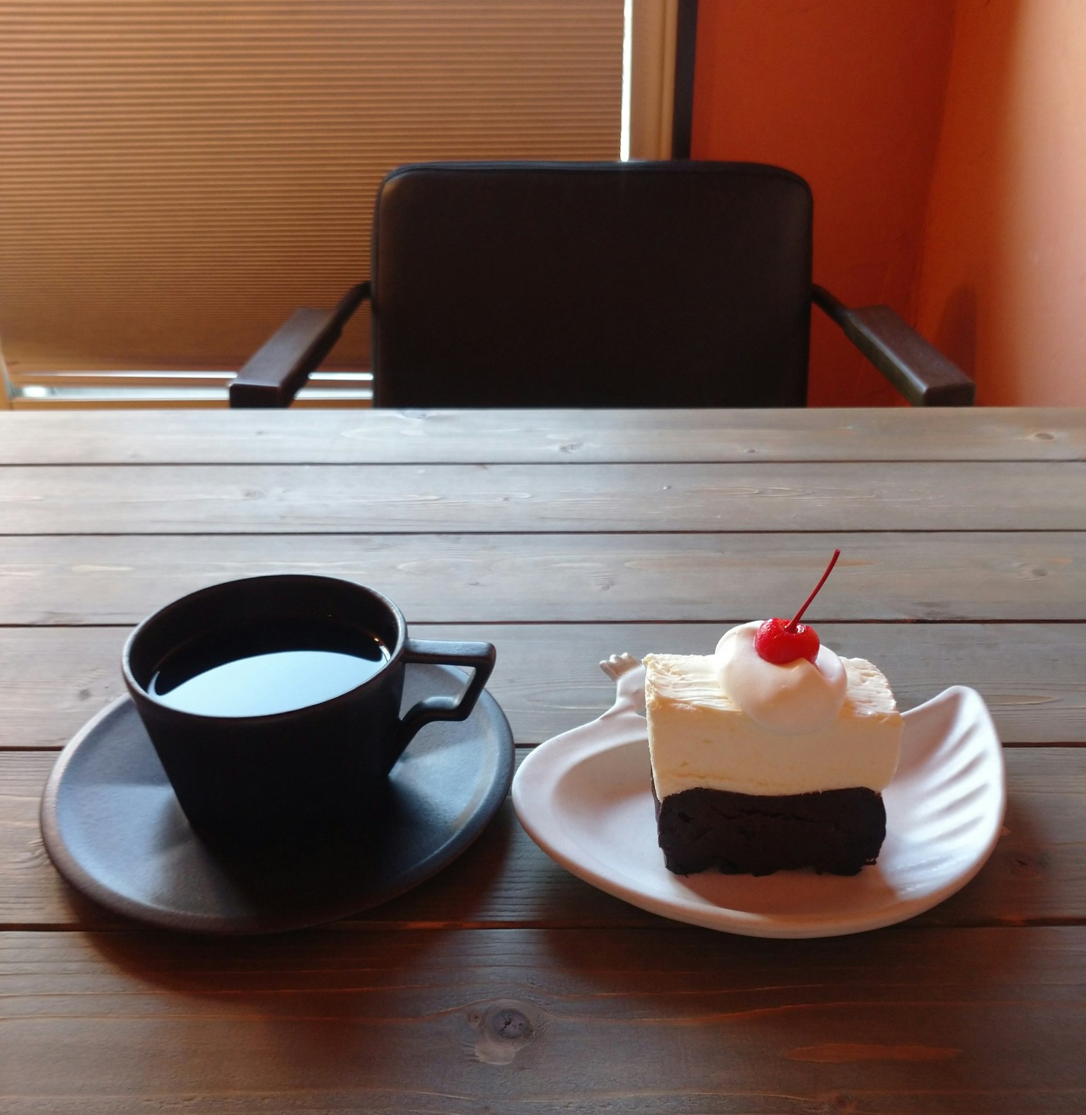 Eine schwarze Tasse Kaffee und ein Stück Kuchen mit Schlagsahne und einer Kirsche auf einem Tisch