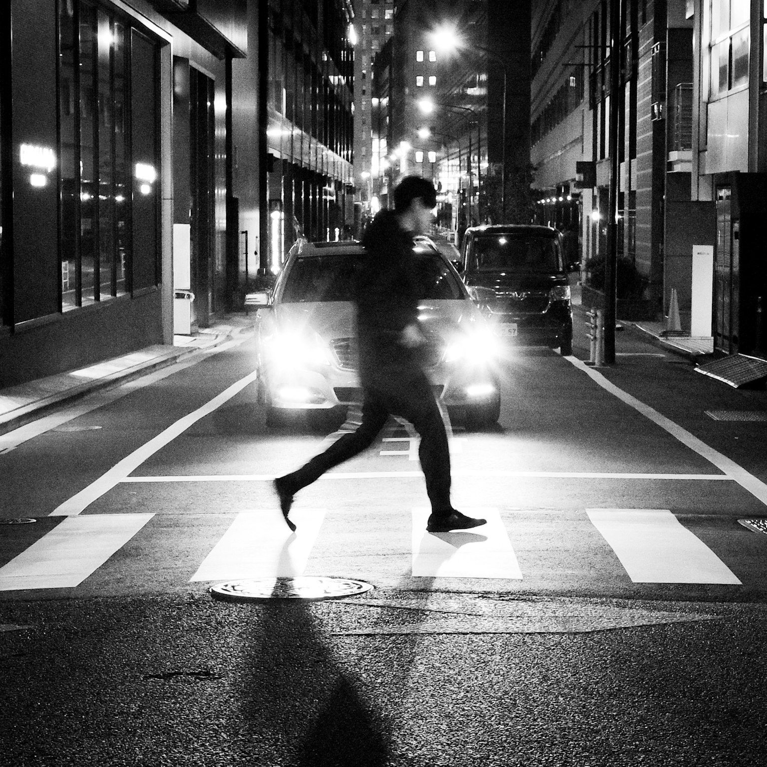 Silhouette of a man walking in a city intersection black and white scene with car headlights shining