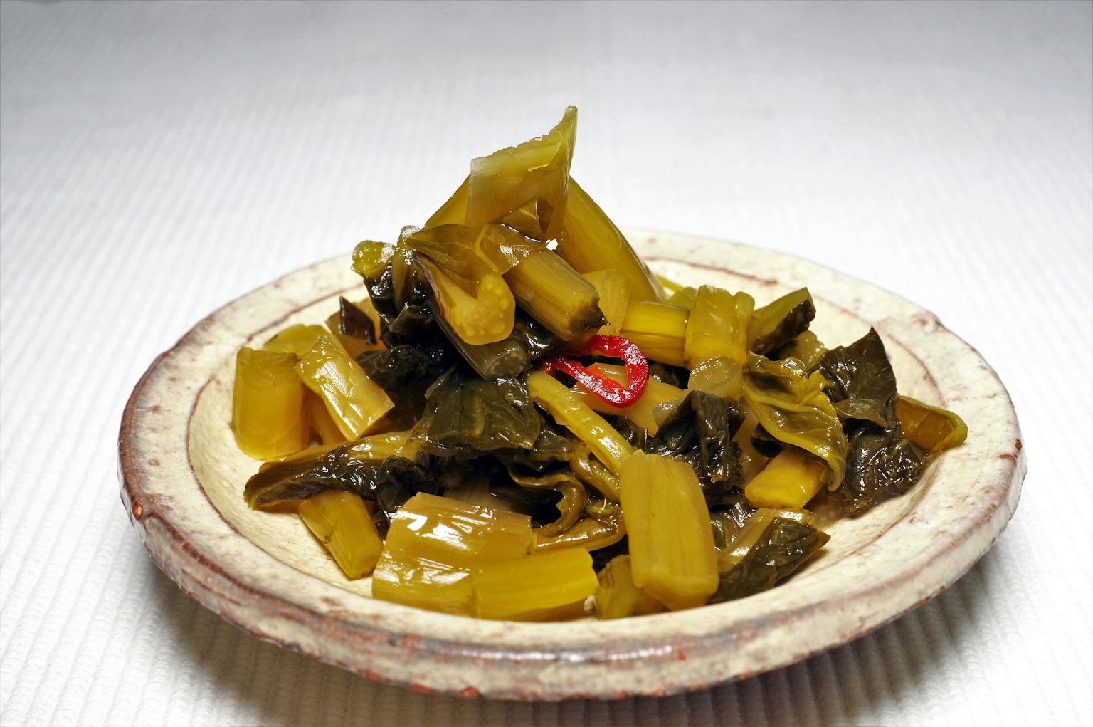 一盤綠色醃製蔬菜，上面裝飾著紅辣椒