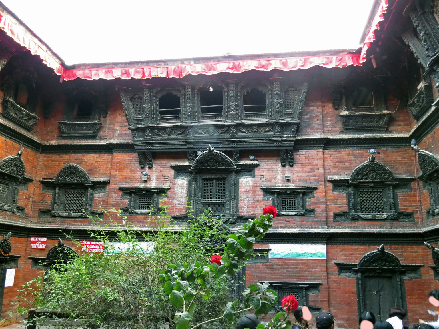 Traditional Nepali architecture featuring decorative windows in a courtyard with red roofs and greenery
