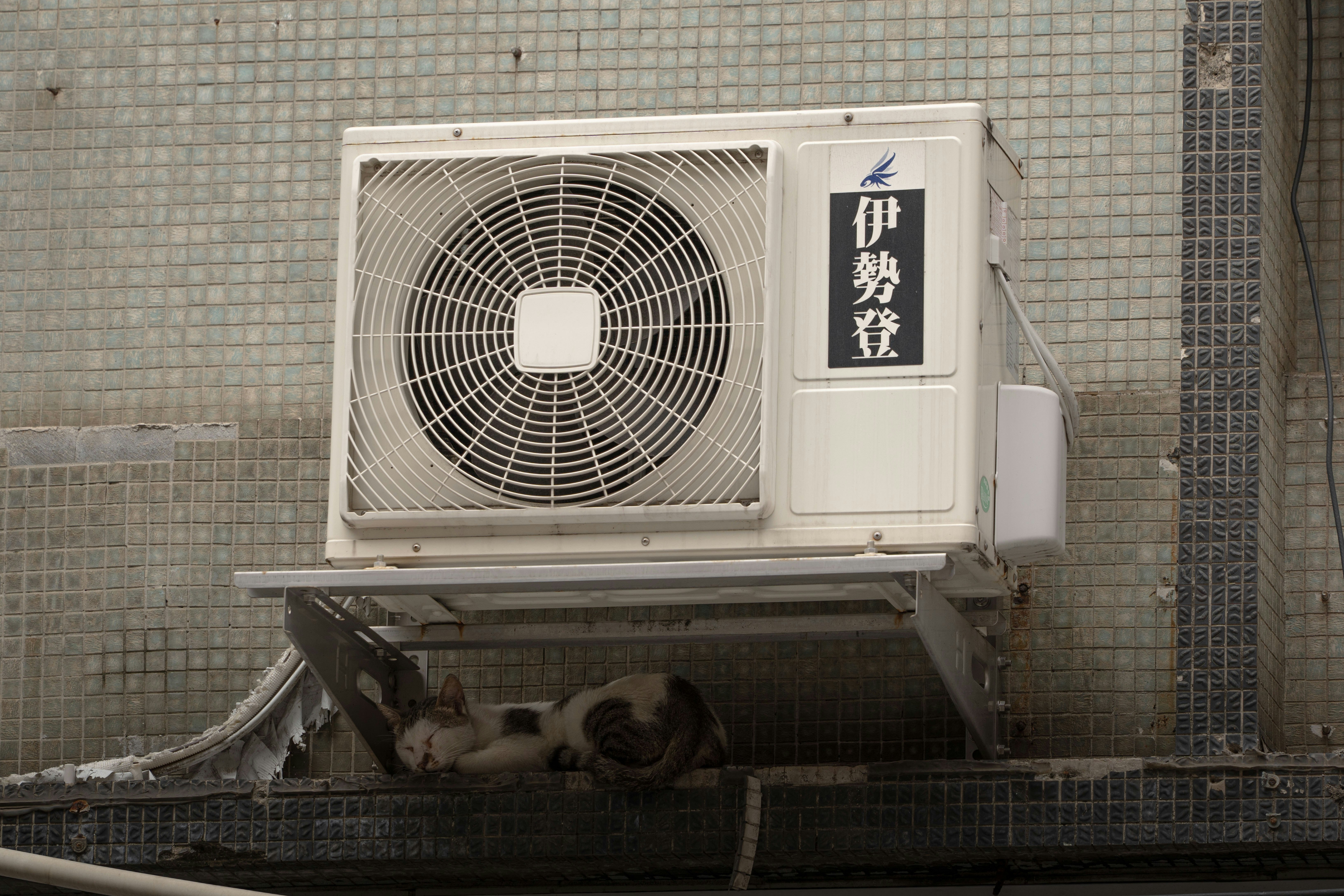 Air conditioning unit mounted on a wall with visible fan and signage