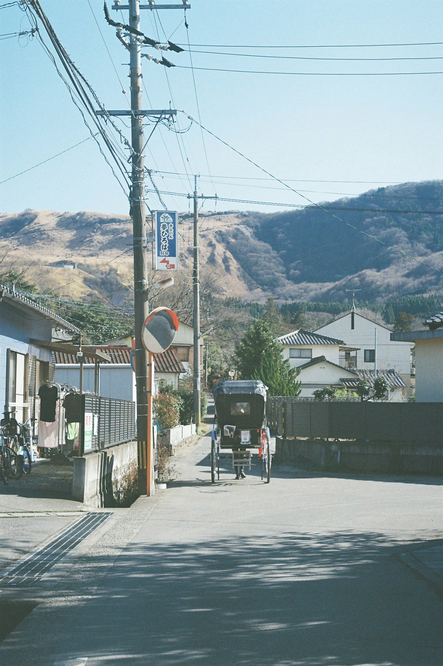 Escena de una tranquila calle residencial japonesa con montañas al fondo postes de luz y casas a lo largo de la carretera