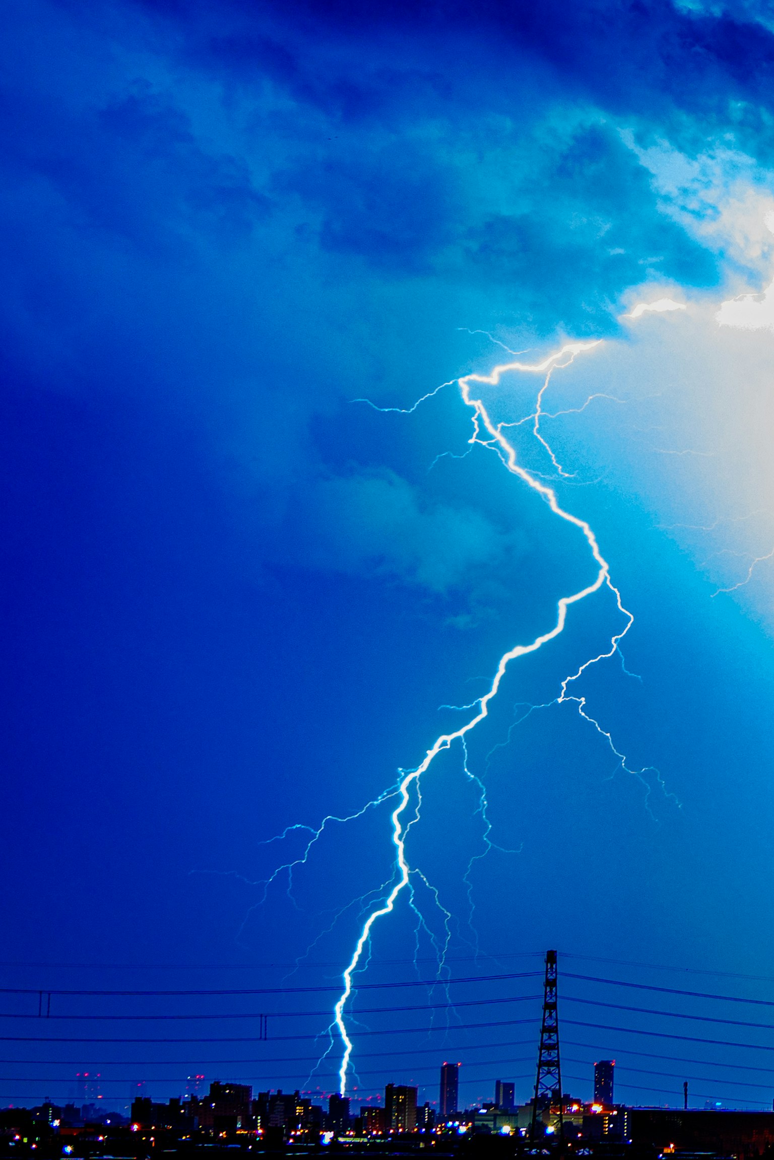 Lightning striking over a city skyline under a blue sky