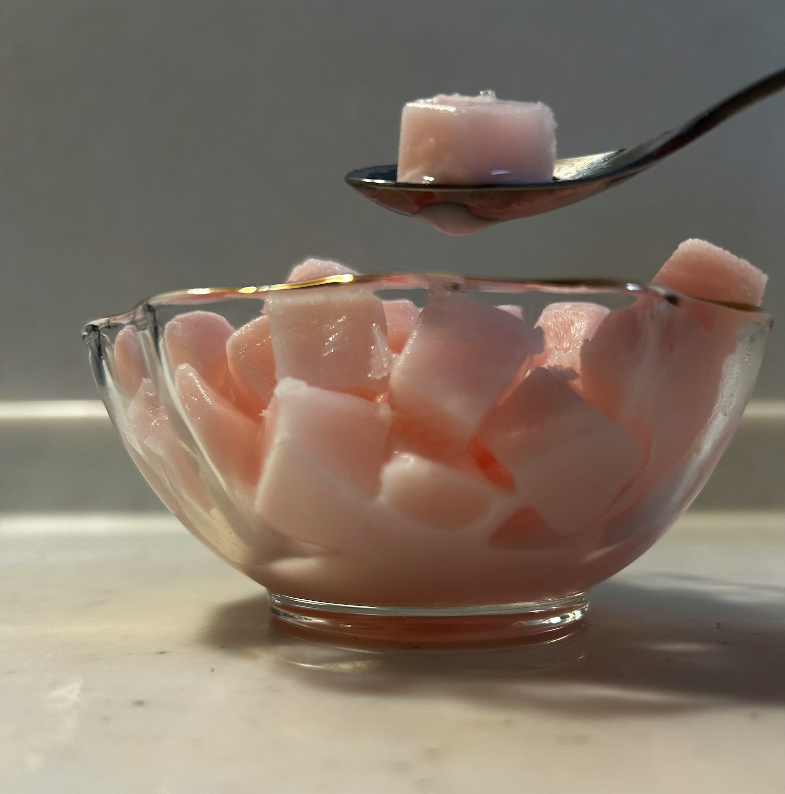 Rosa würfelförmiger Zucker in einer klaren Glasschüssel mit einem Löffel