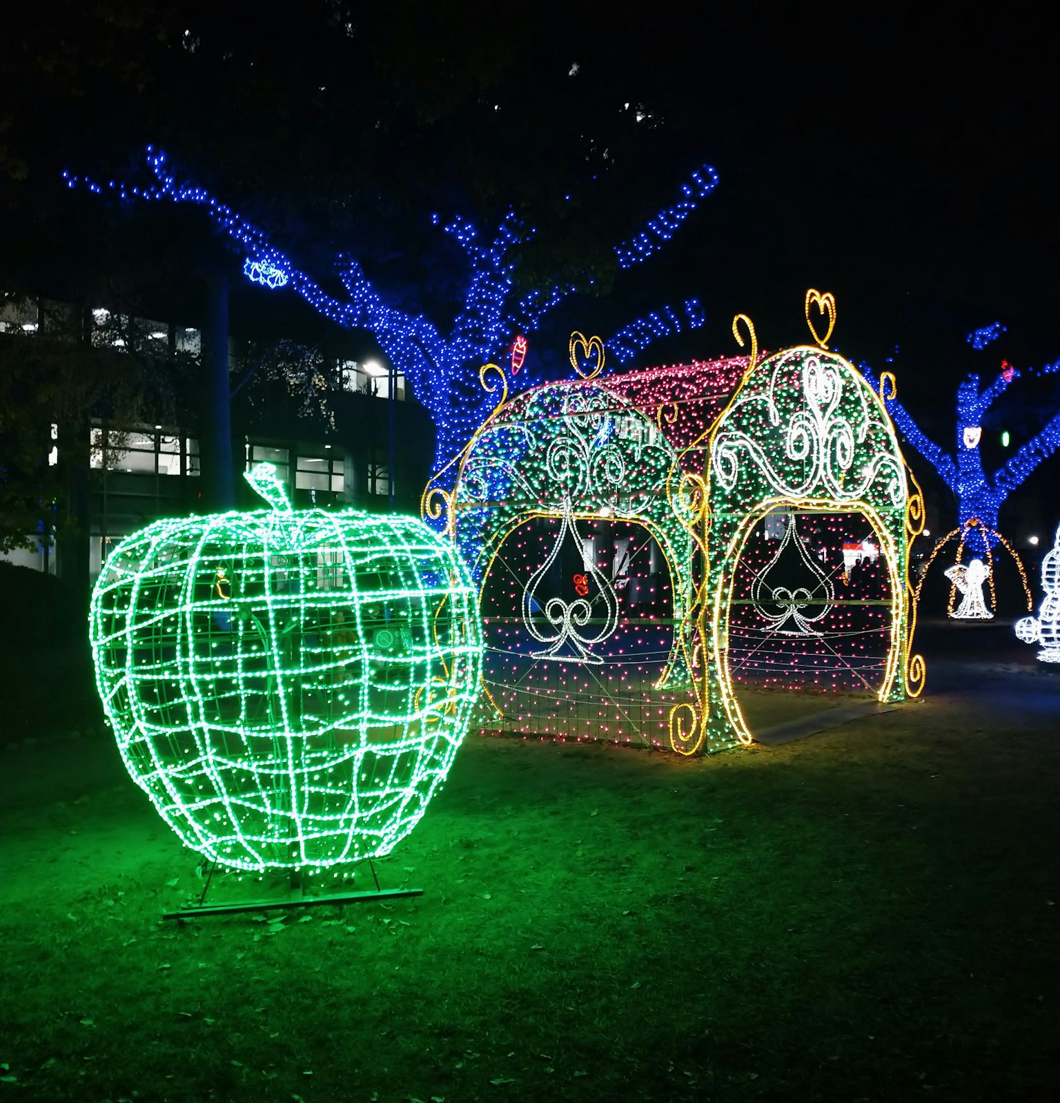 Scultura di mela verde illuminata e strutture decorate colorate in un parco notturno