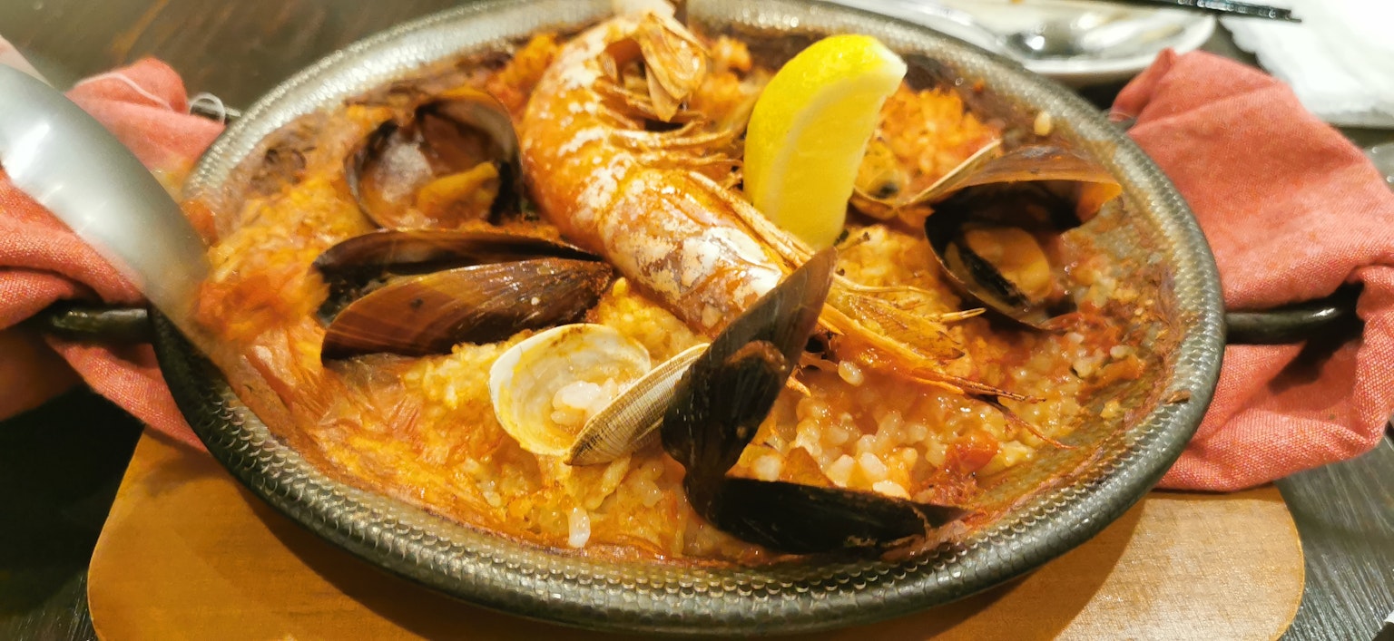 Paella de mariscos servida en un plato con camarones y mejillones decorada con limón
