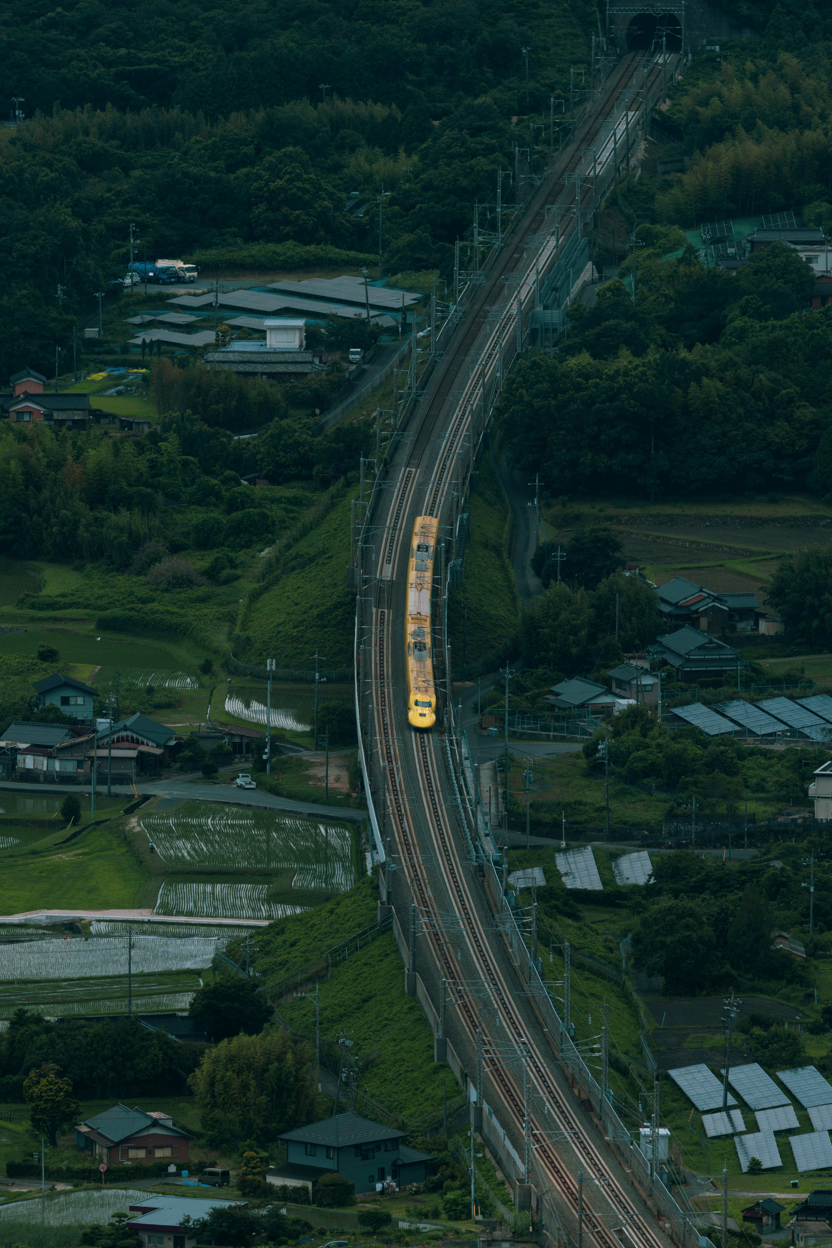 山あいの集落を貫く長い直線道路を走る列車の俯瞰