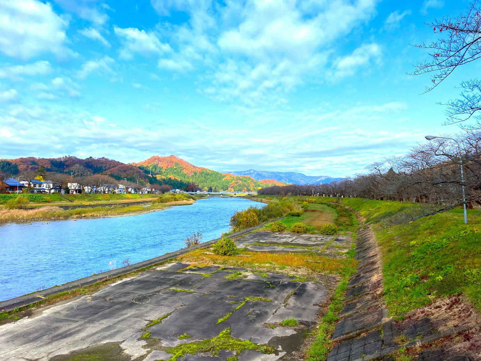 Vista panoramica di un fiume con prati verdi e montagne sotto un cielo blu