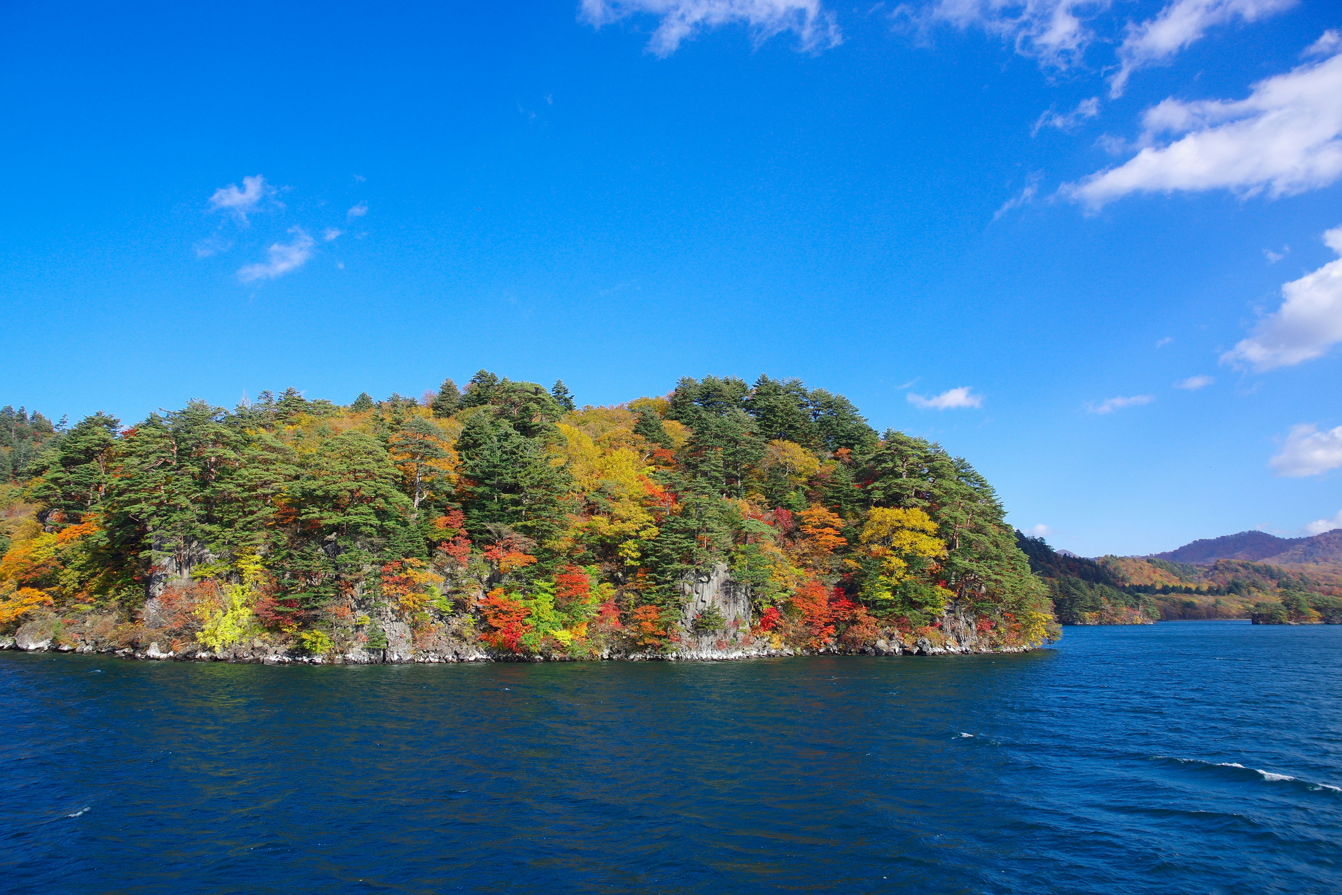湖畔に迫る紅葉の森と青空
