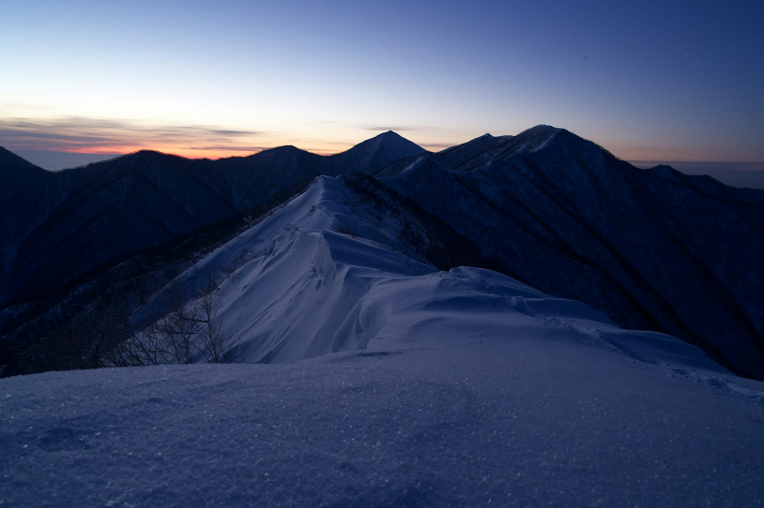 Cresta montañosa cubierta de nieve con cielo al anochecer