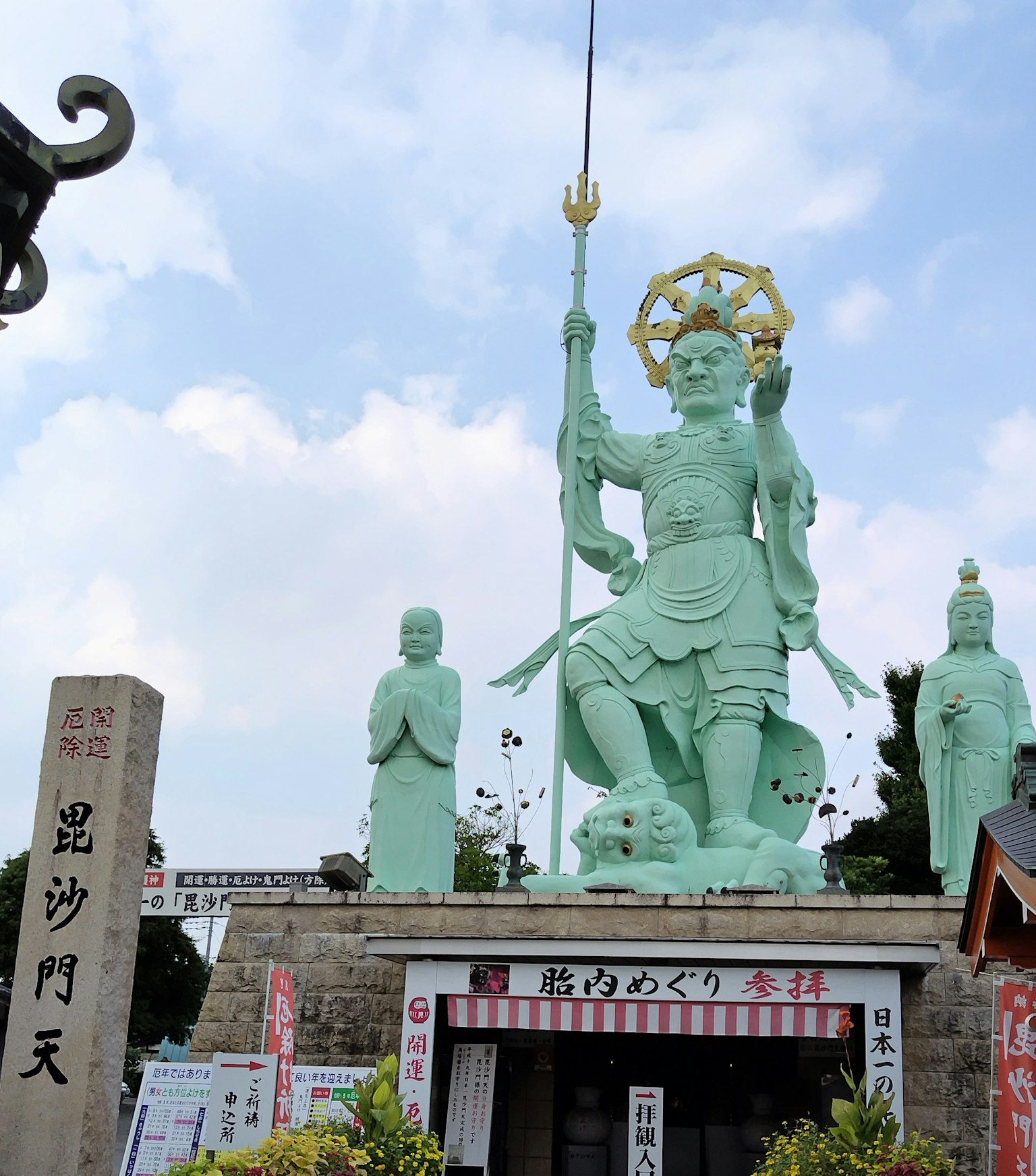 青铜神像矗立在神社入口，周围有小雕像