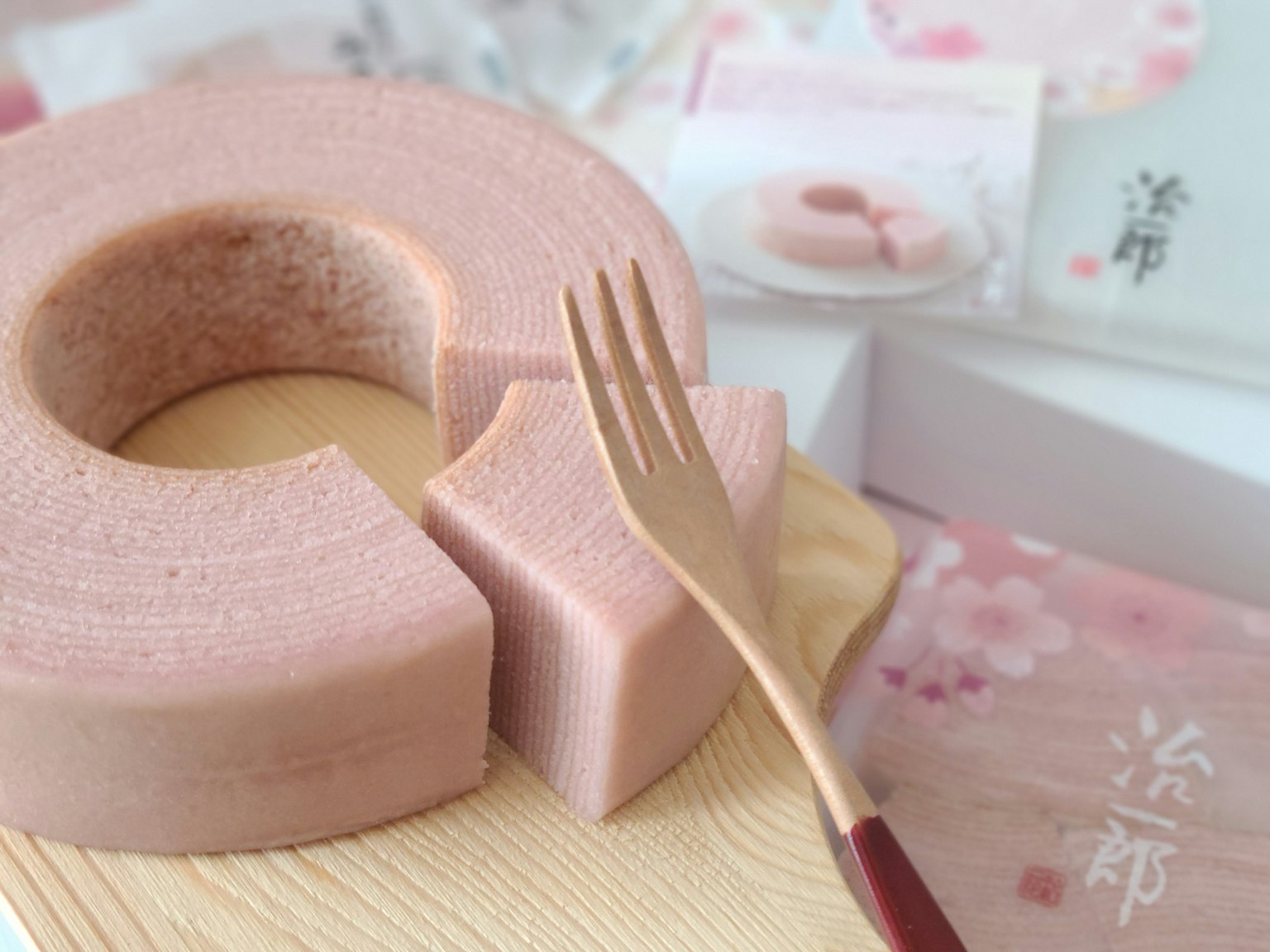 Imagen de un Baumkuchen rosa con un tenedor en un plato de madera mostrando una rebanada