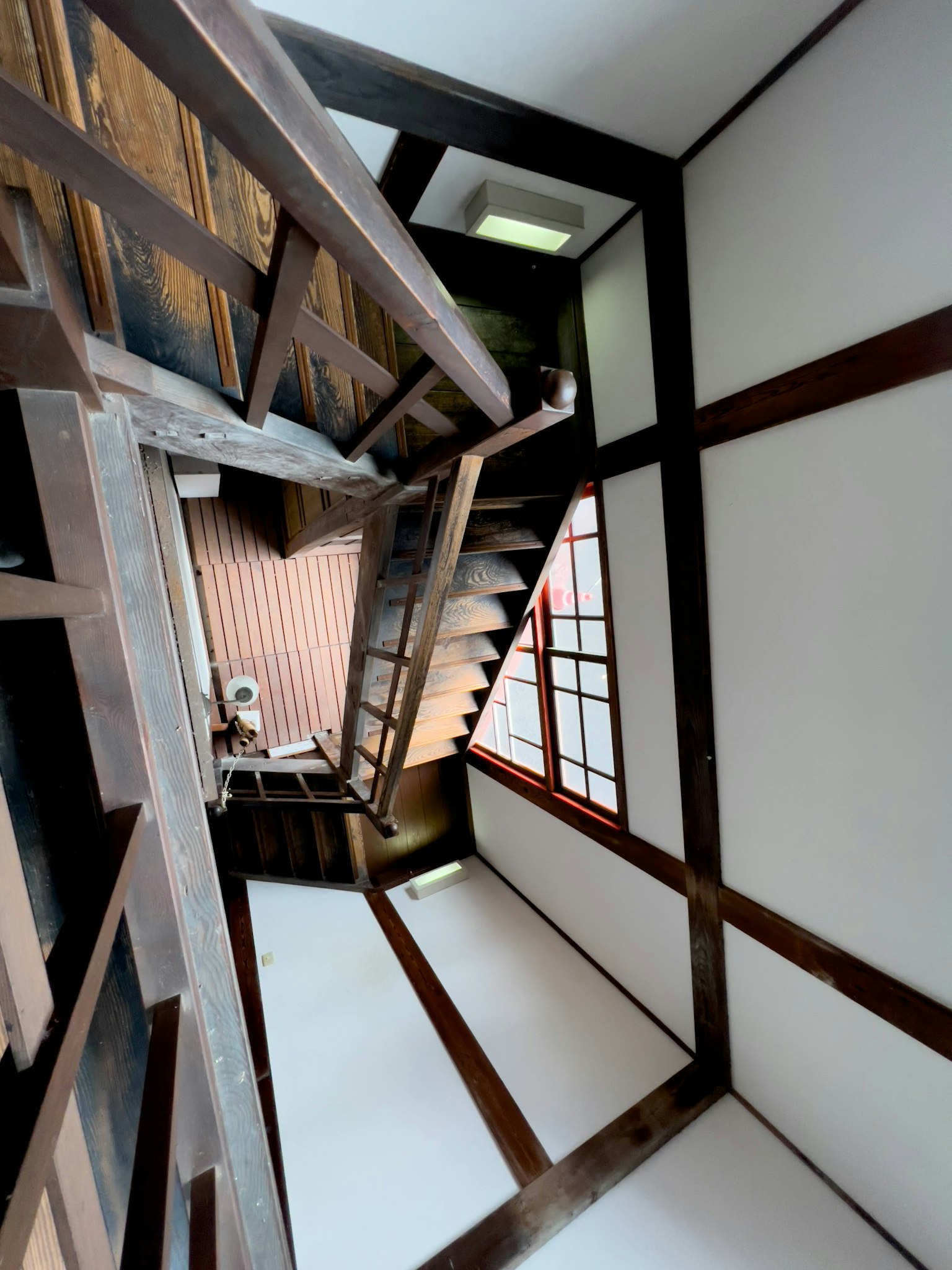 Vue du haut d'un escalier avec des rampes en bois et des murs blancs