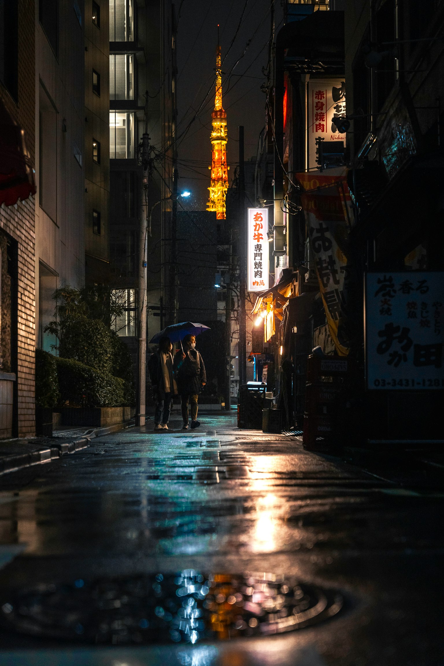 Couple walking in a Tokyo alley at night with Tokyo Tower in the background