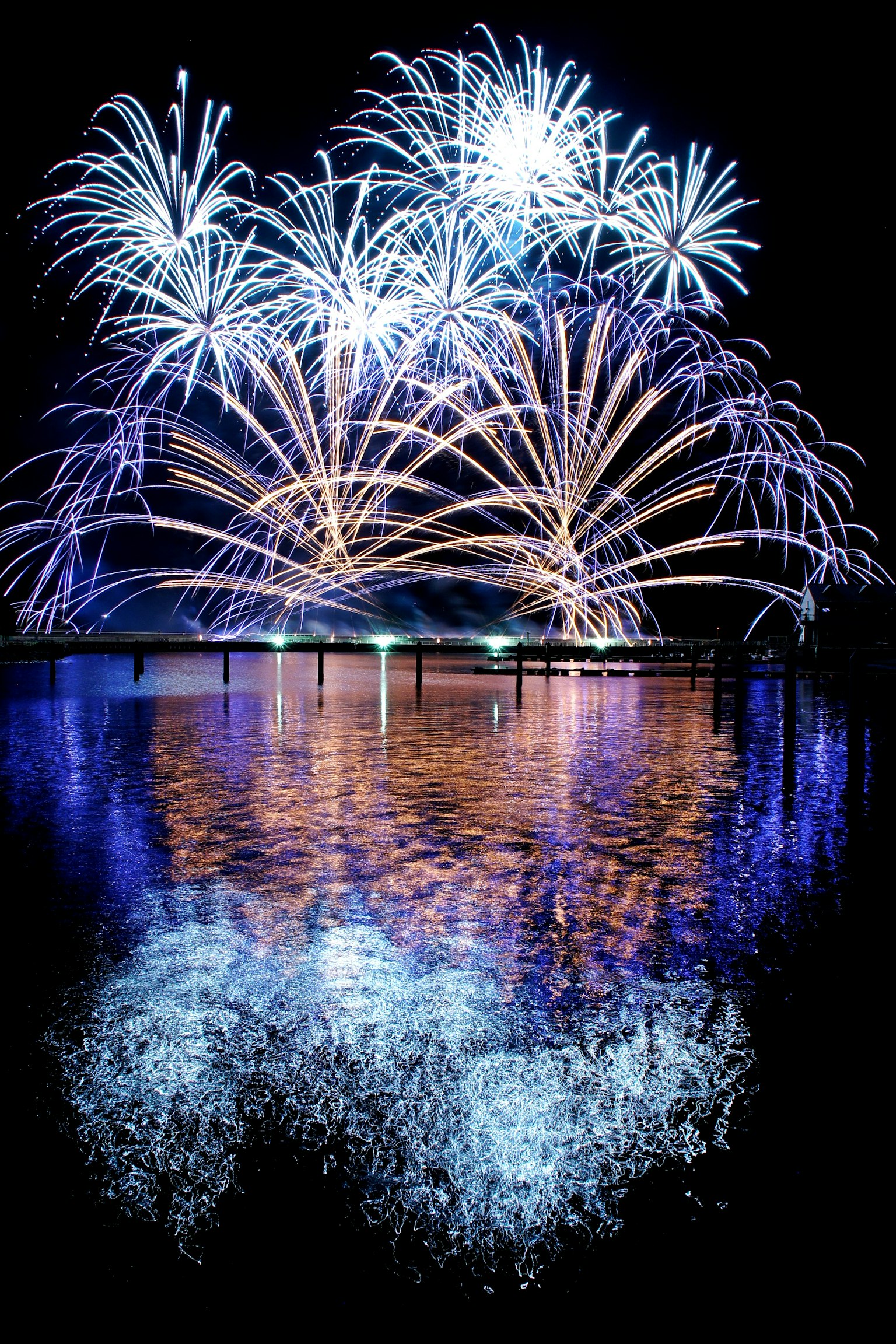 夜空中綻放的生動藍色煙花與水面倒影