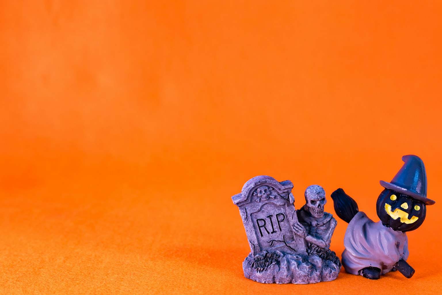 Une pierre tombale violette et un personnage de citrouille d'Halloween sur un fond orange