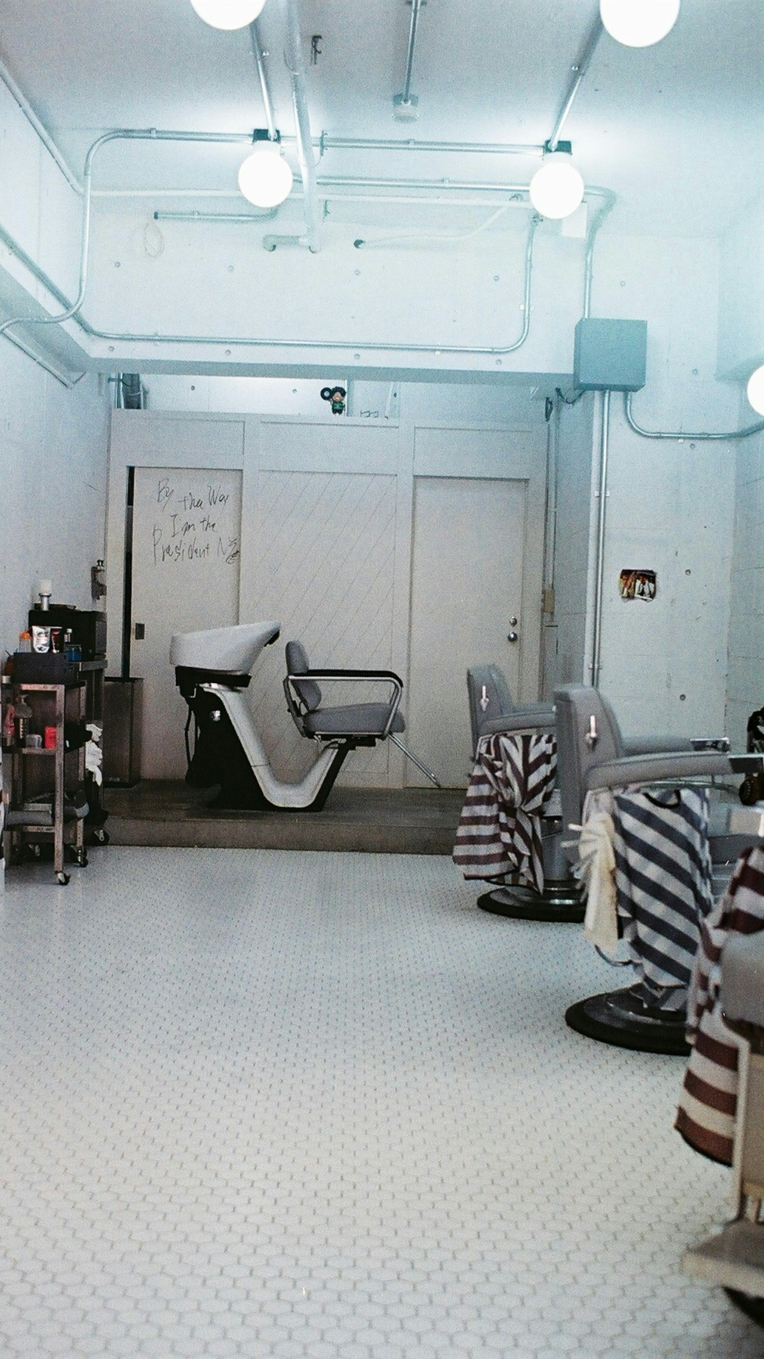 Interior de una barbería con paredes y suelo blancos sillas a rayas dispuestas en un diseño limpio y simple