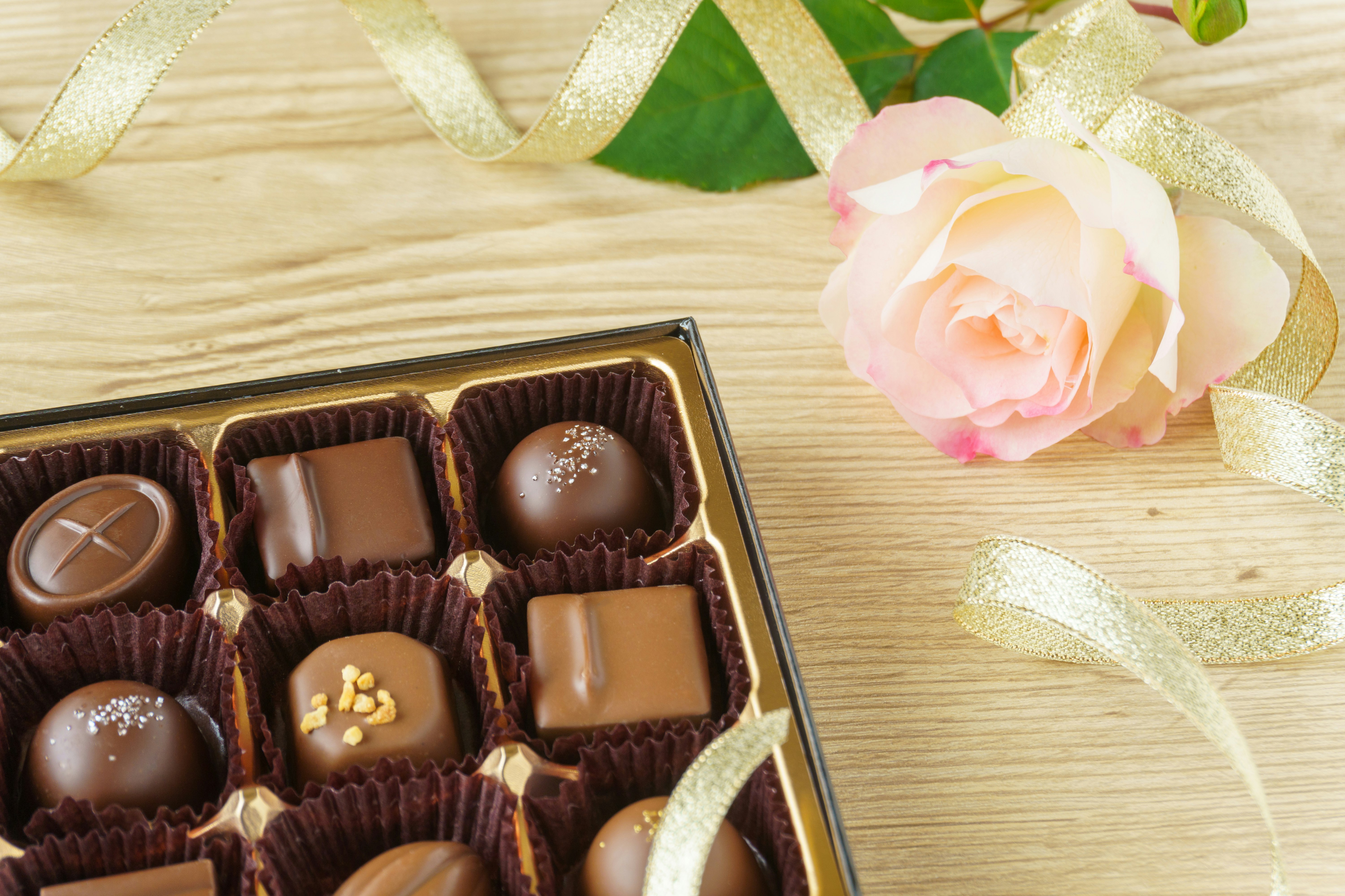 Schokoladenpralinen-Box auf Holzuntergrund mit rosa Rosen-Deko