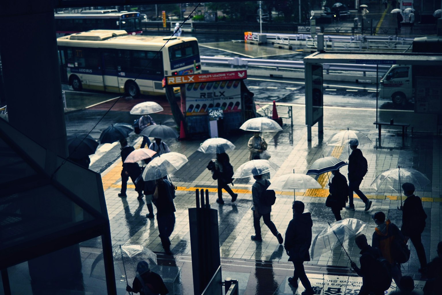 People walking in the rain with umbrellas near a bus stop