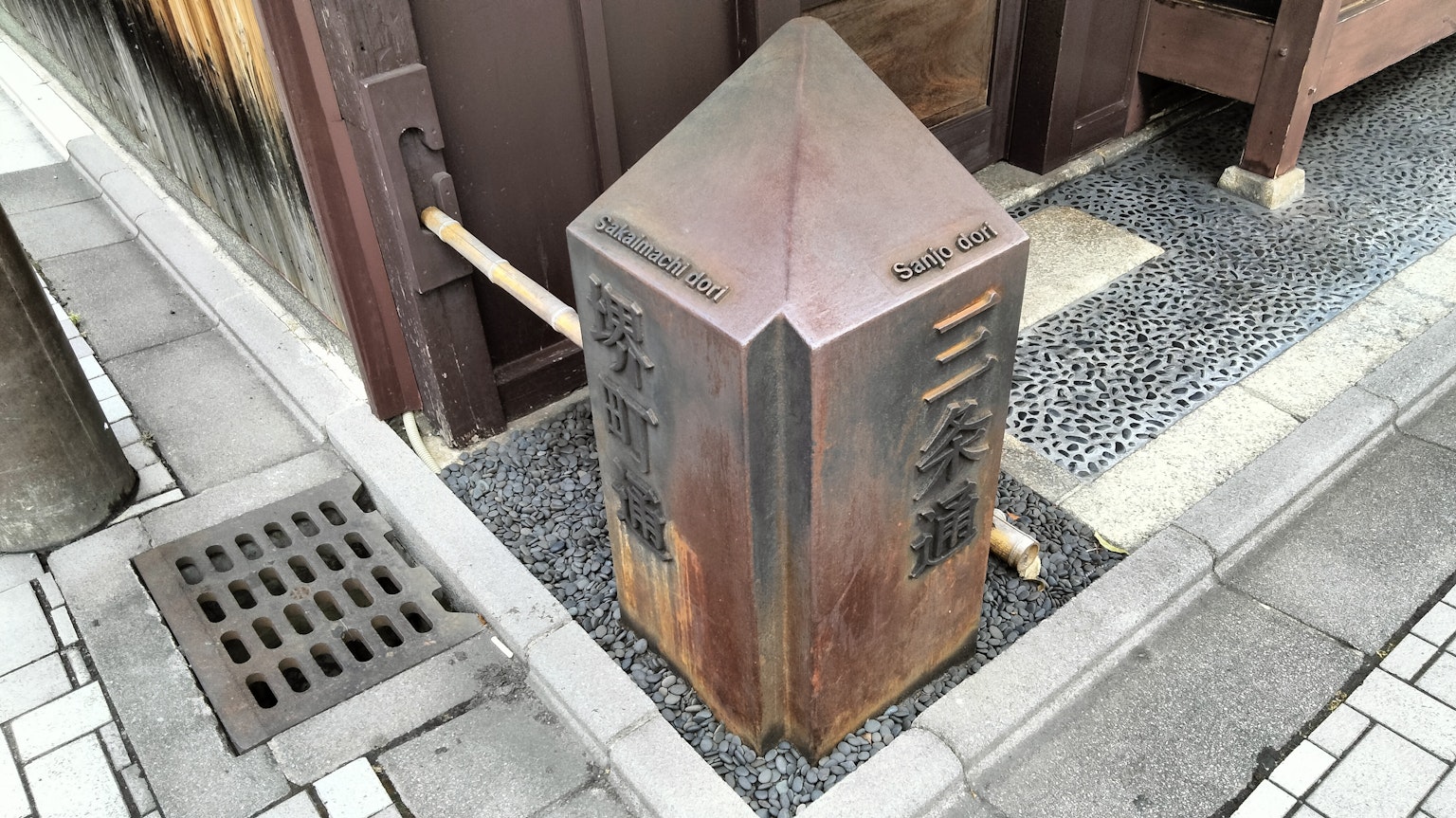 Ein vintage Metallpfeiler steht an einer Straßenecke umgeben von Steinpflaster und Holzstrukturen