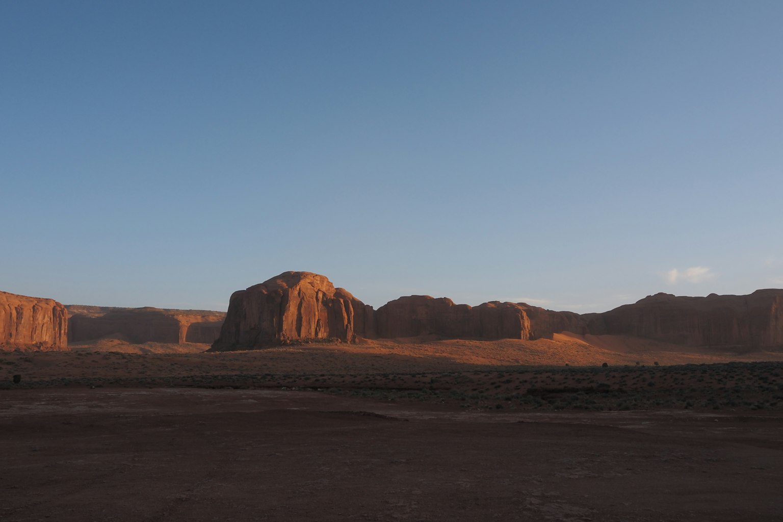 Vast desert landscape with majestic rock formations illuminated by sunset