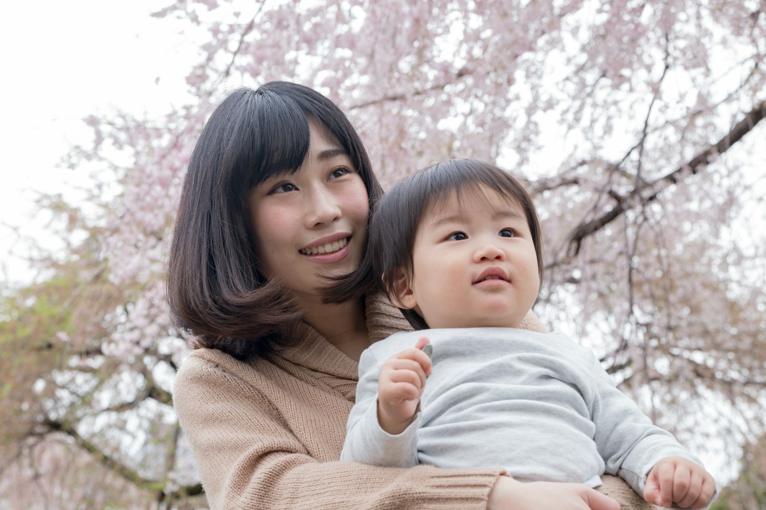 Smiling mother holding child under cherry blossom trees