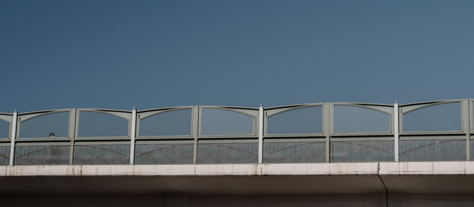 Section of a bridge with white railings under a blue sky