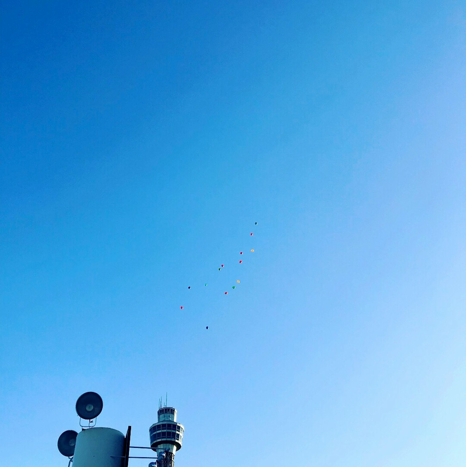 A view of balloons floating in the blue sky with a communication tower