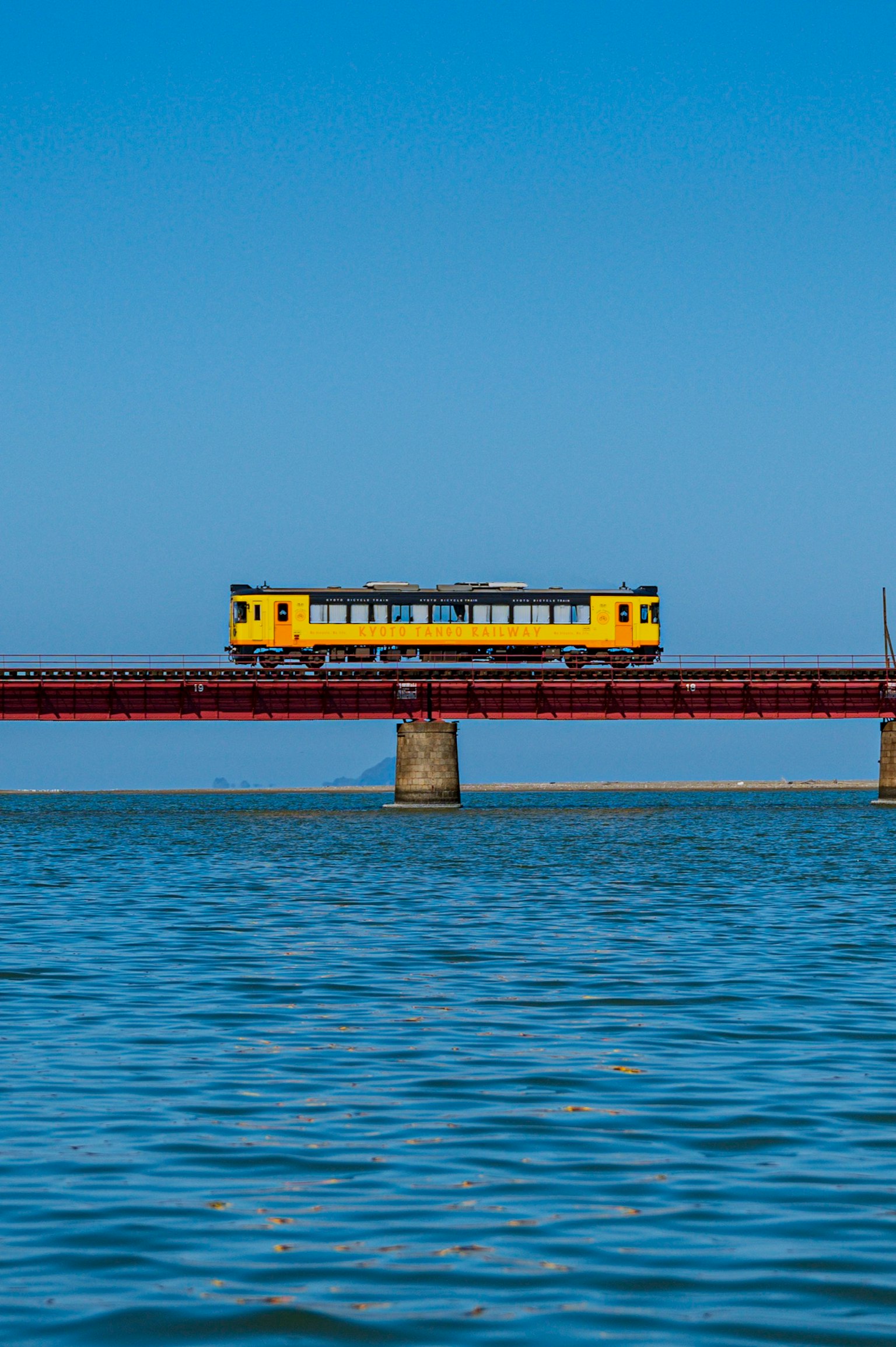 Train jaune traversant un pont rouge au-dessus de l'eau