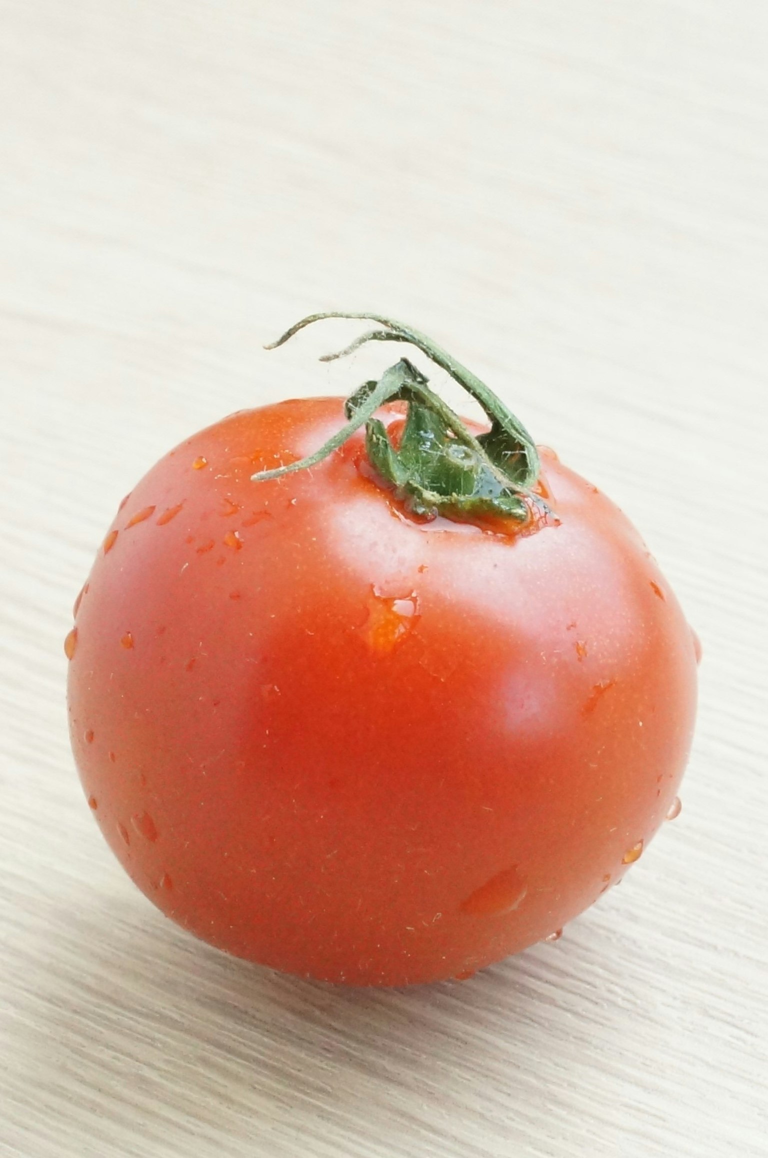 Un tomate fresco con gotas de agua está sobre una mesa de madera