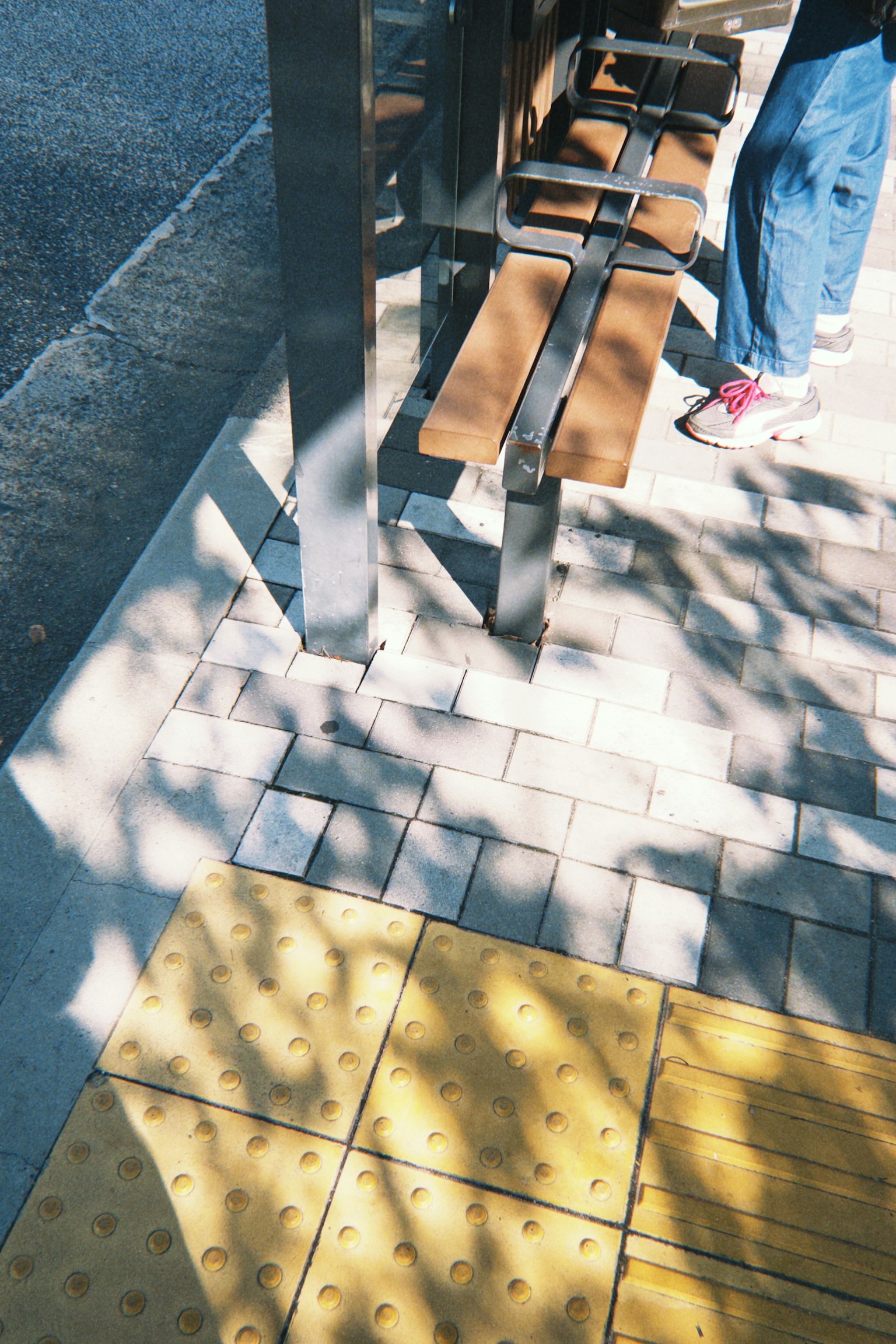 Photo of a sidewalk with a bench and shadows