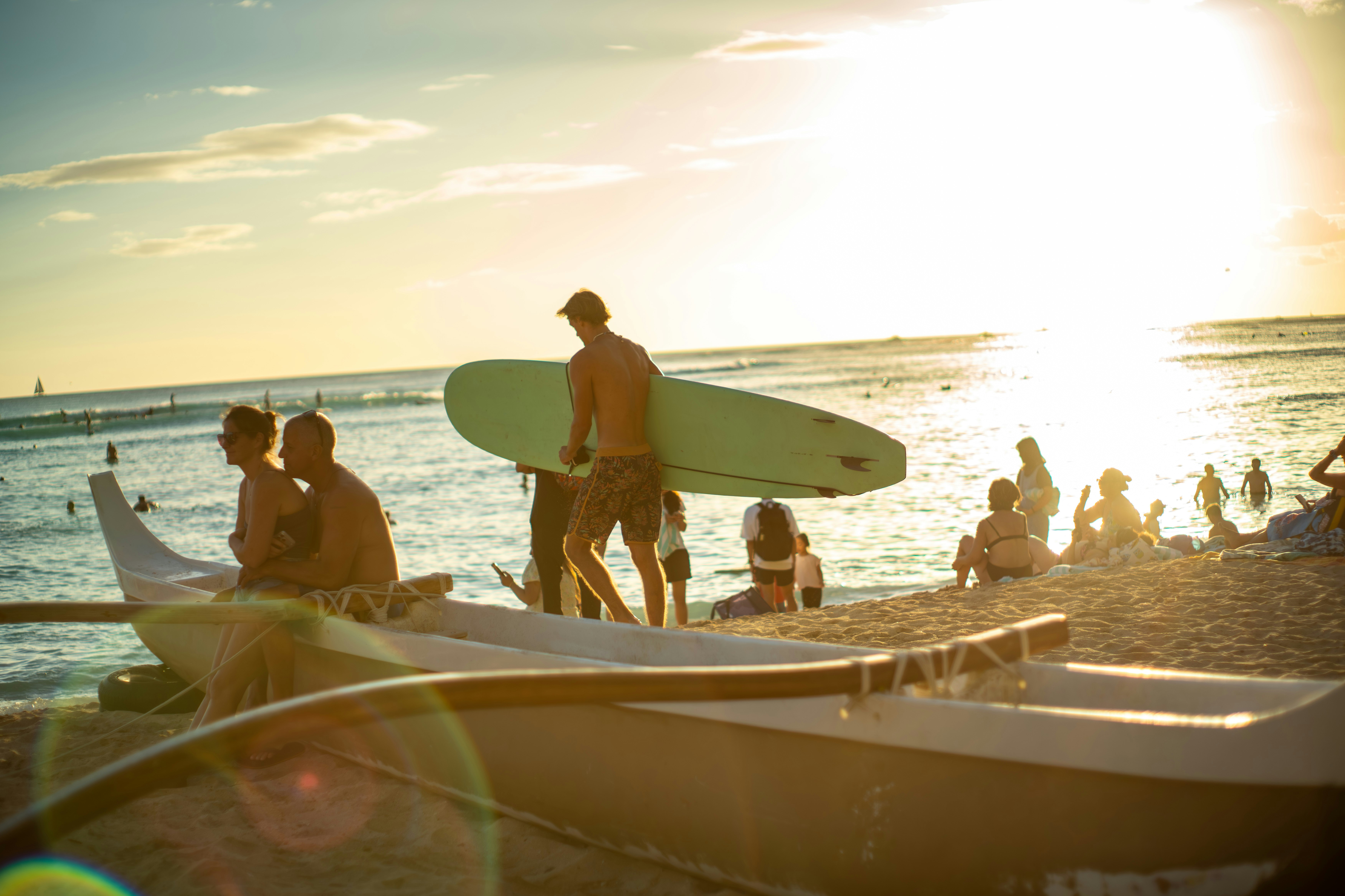 海辺でサーフボードを持つ人々の夕暮れのビーチシーン
