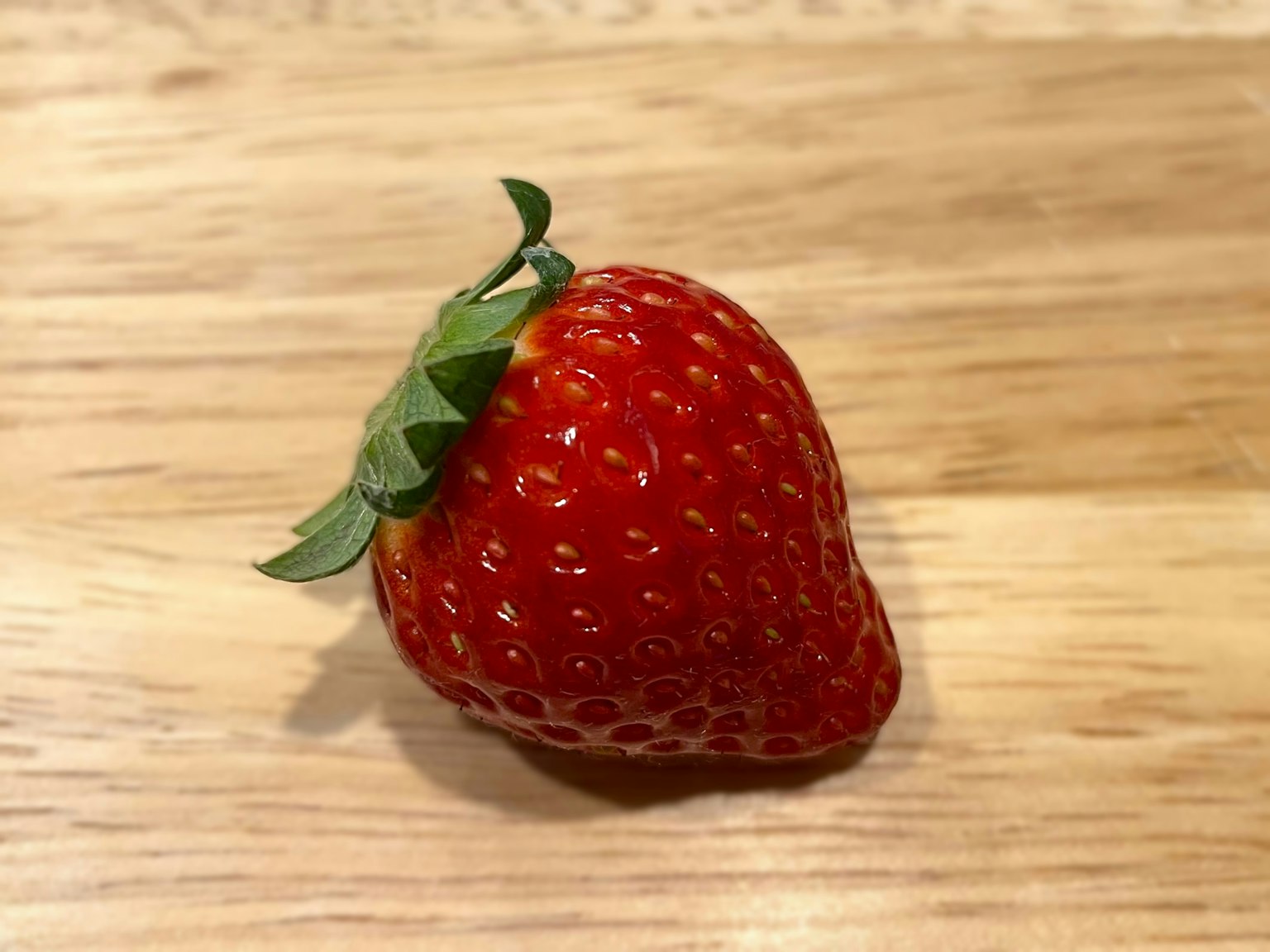 A vibrant red strawberry resting on a wooden table